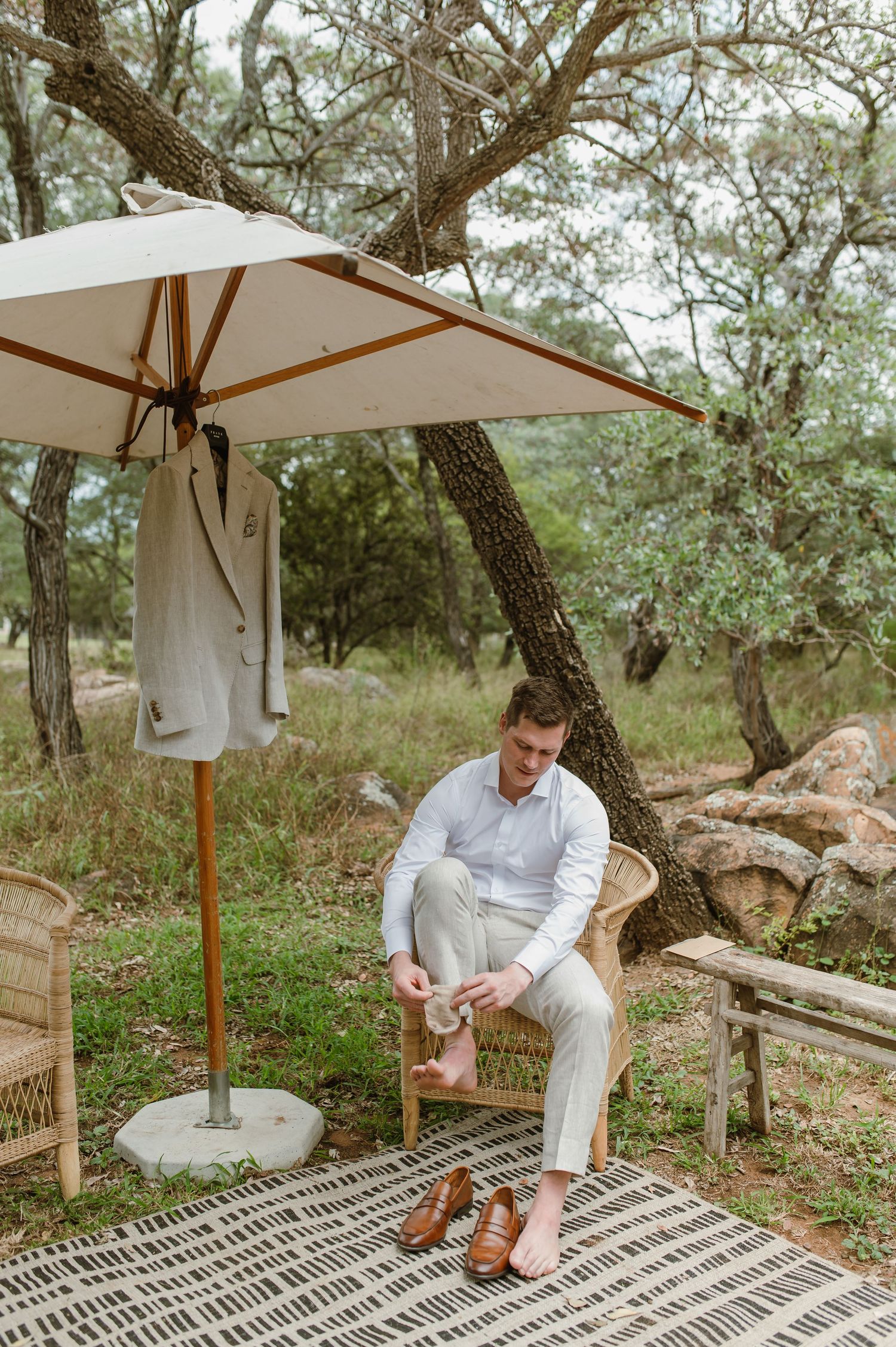 Outdoor seating area under white umbrella with rustic decor and natural woodland backdrop.