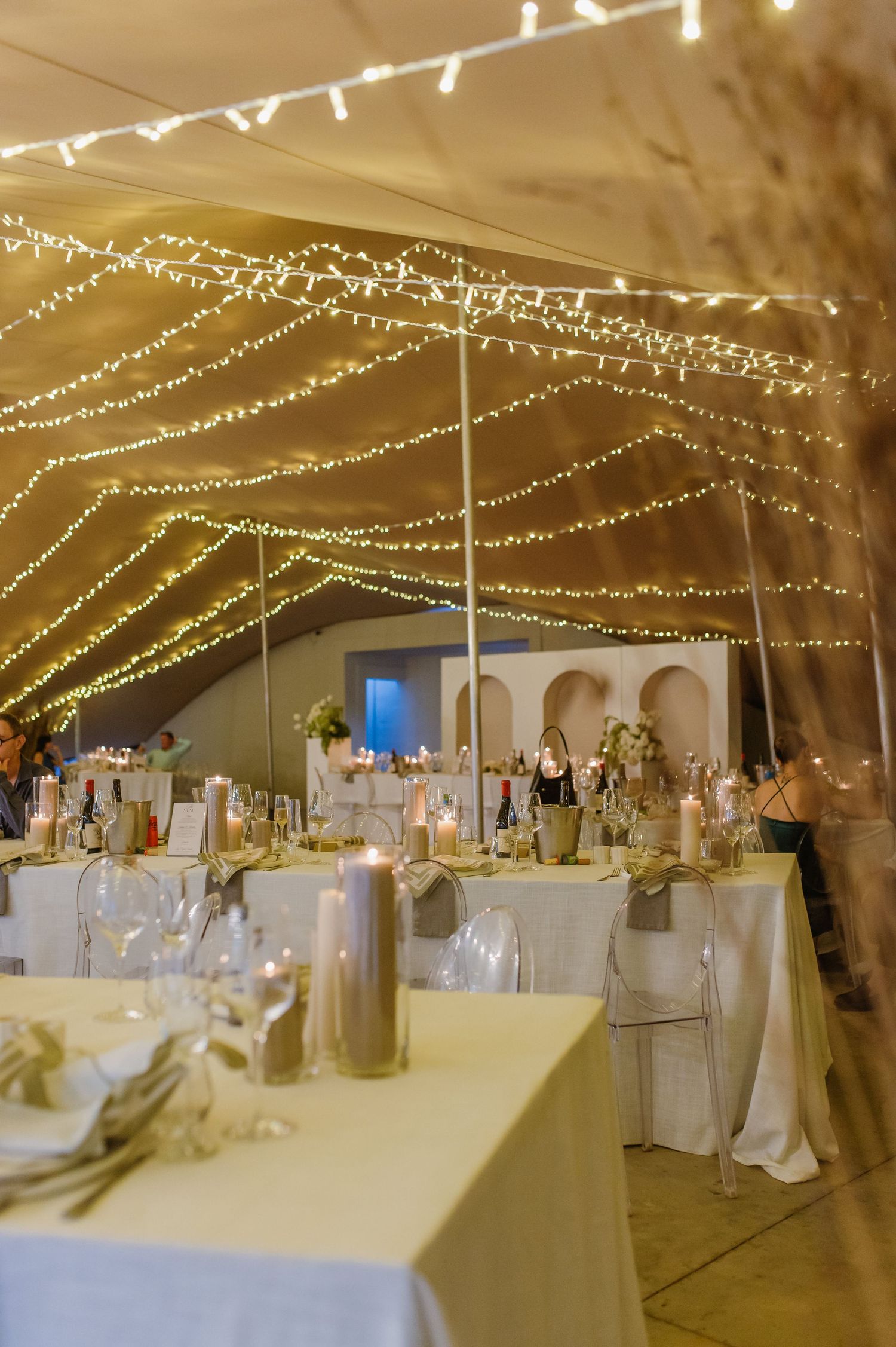 Wedding reception venue decorated with romantic string lights and white table settings under an elegant tent.