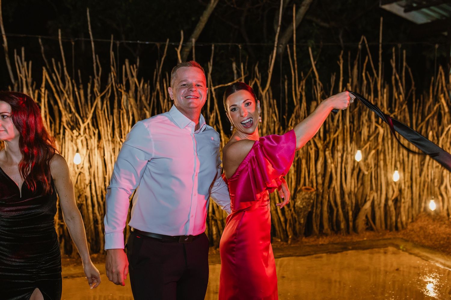 Woman in bright pink dress dancing joyfully with a man in a white shirt at a wedding reception.