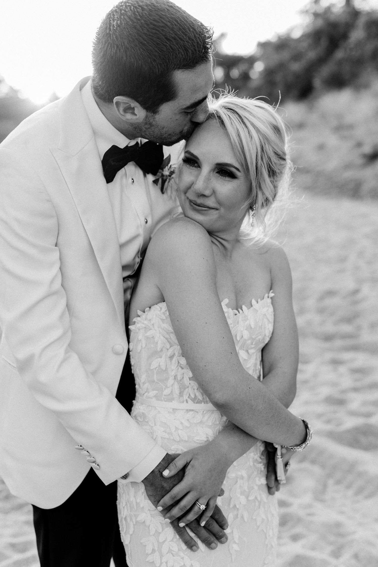 Romantic beach wedding couple embraces during sunset photoshoot in golden light.
