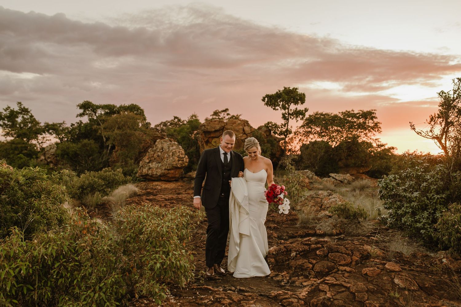 Wide landscape shot of newlyweds posing on rocky terrain during sunset.