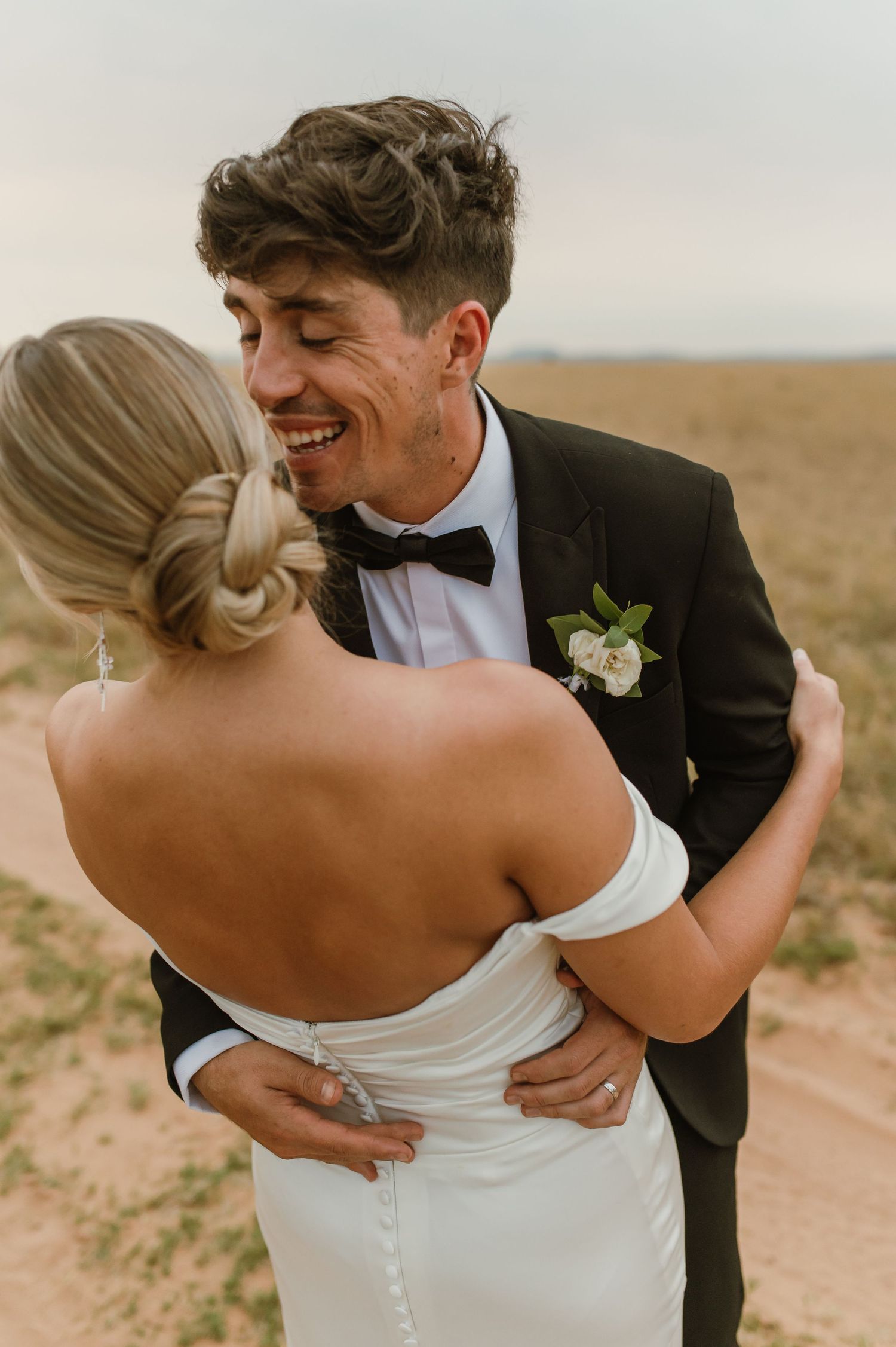 Candid wedding moments showing joyful couple on dirt path through field.