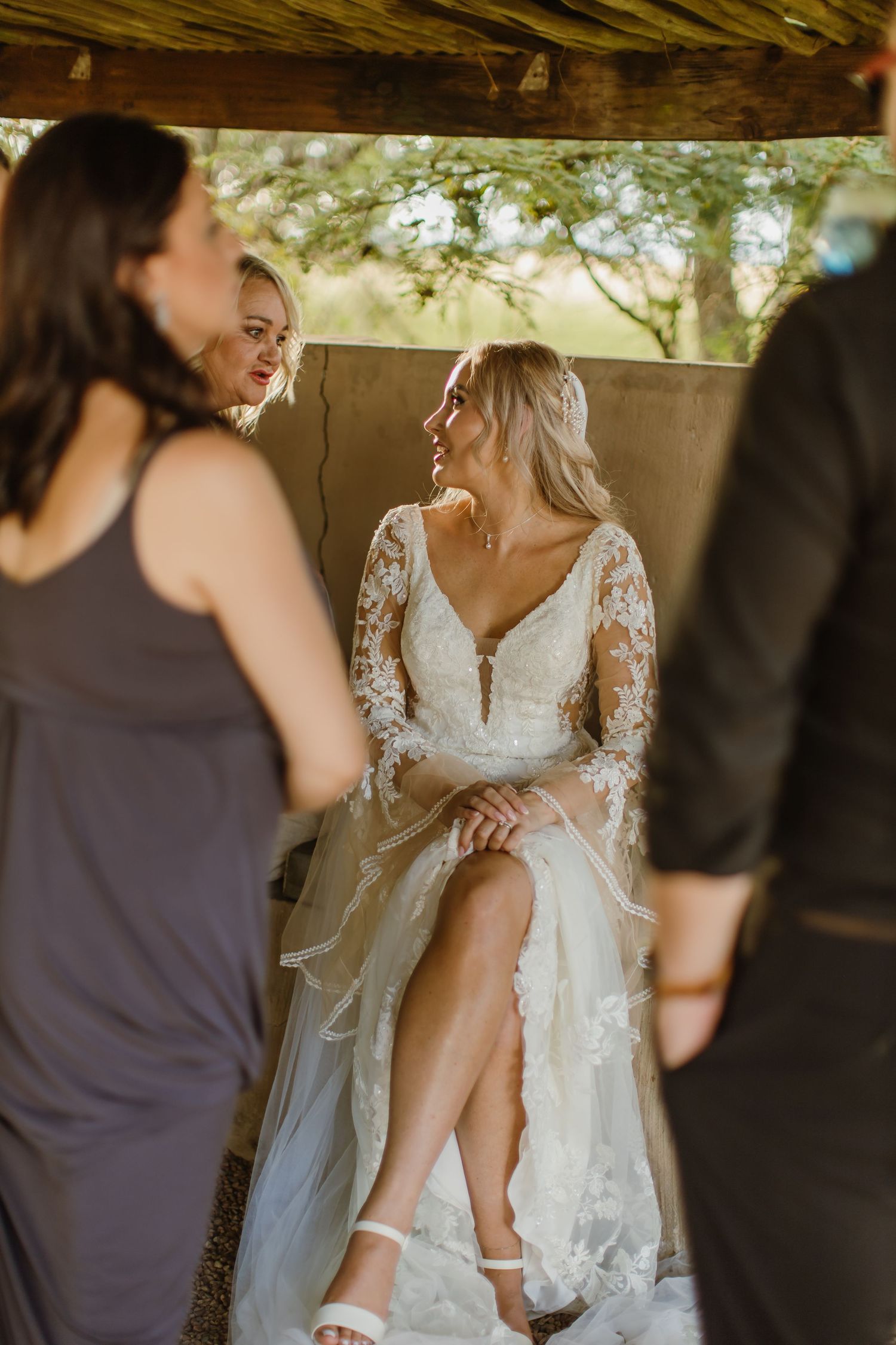 Elegant lace wedding dress details being adjusted under a rustic wooden structure.
