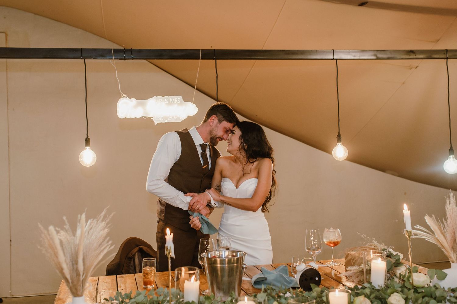 Wedding reception guests dancing and celebrating under a tent with string lights and romantic ambiance.
