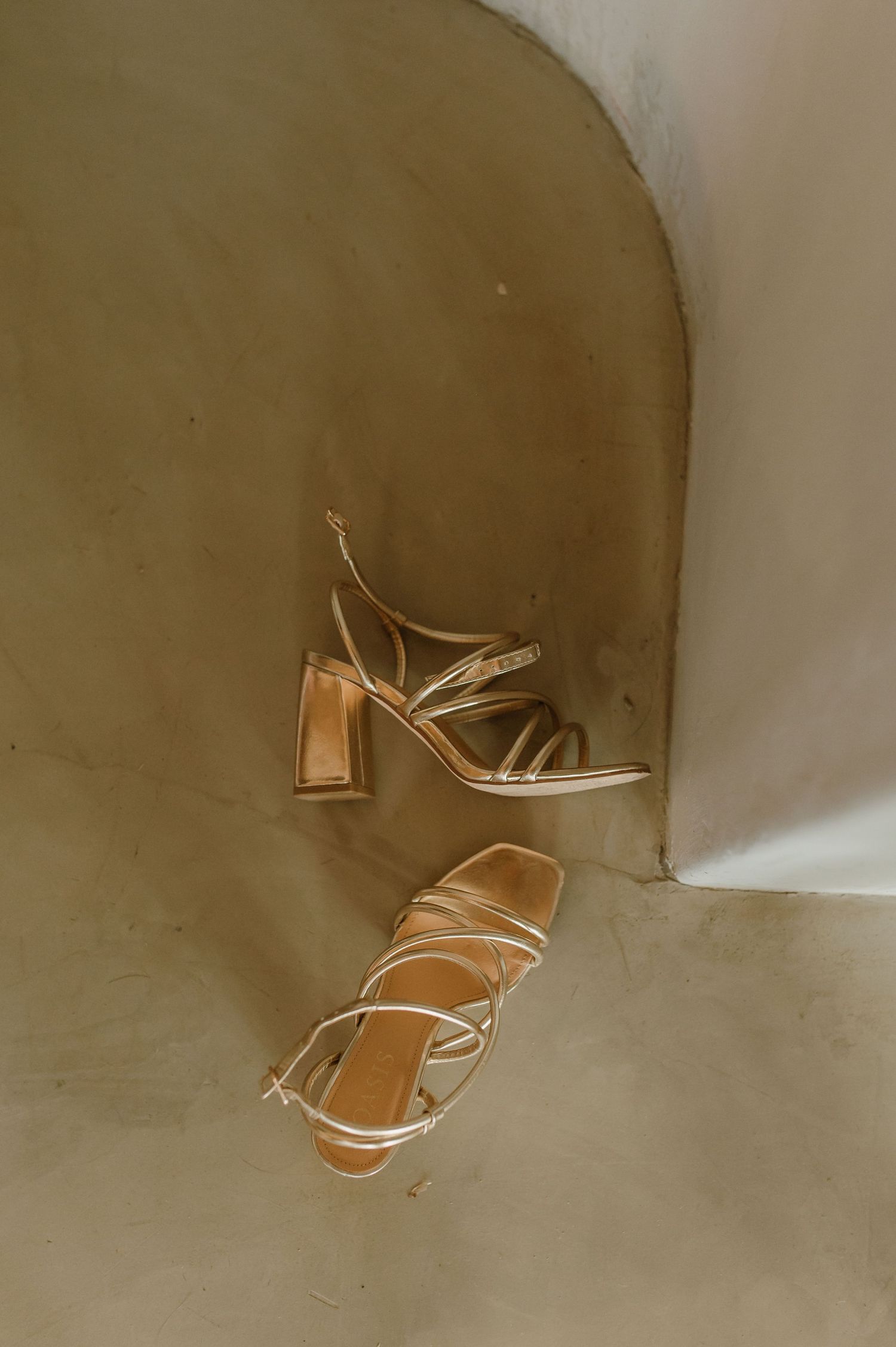 A sequence of a gold high heel shoe falling and spinning against a beige wall.