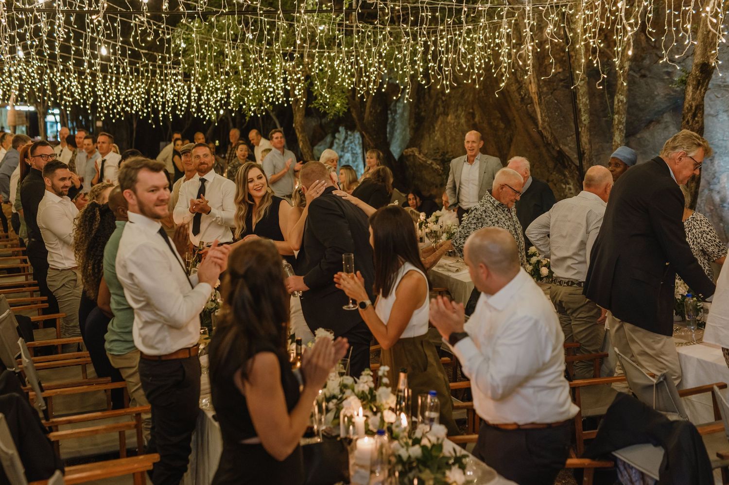 Guests enjoying an outdoor wedding reception under romantic string light canopy.
