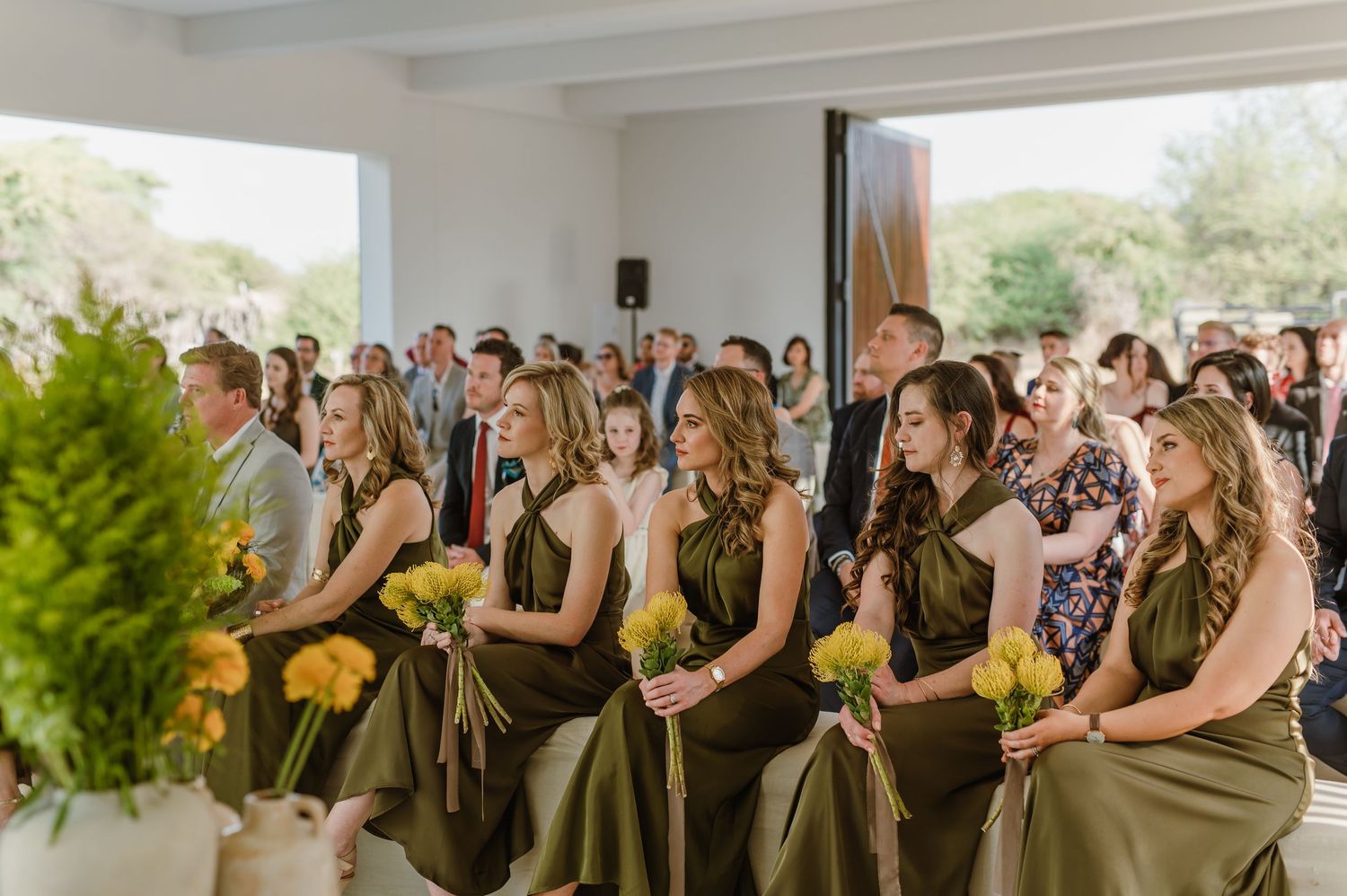 Wedding party members in olive green dresses stand in formation during ceremony.