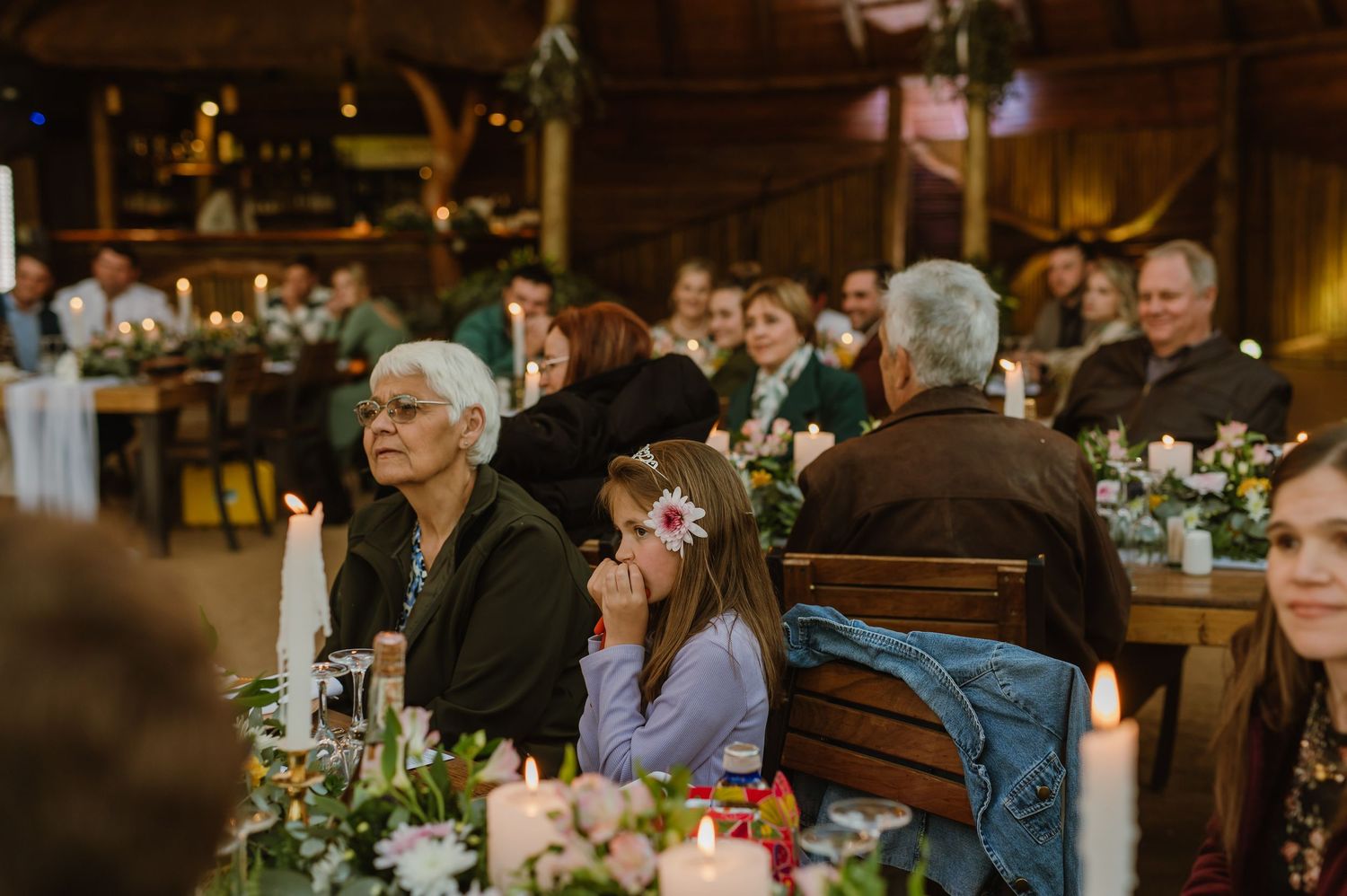 Wedding guests enjoying dinner at long wooden tables under warm indoor lighting.
