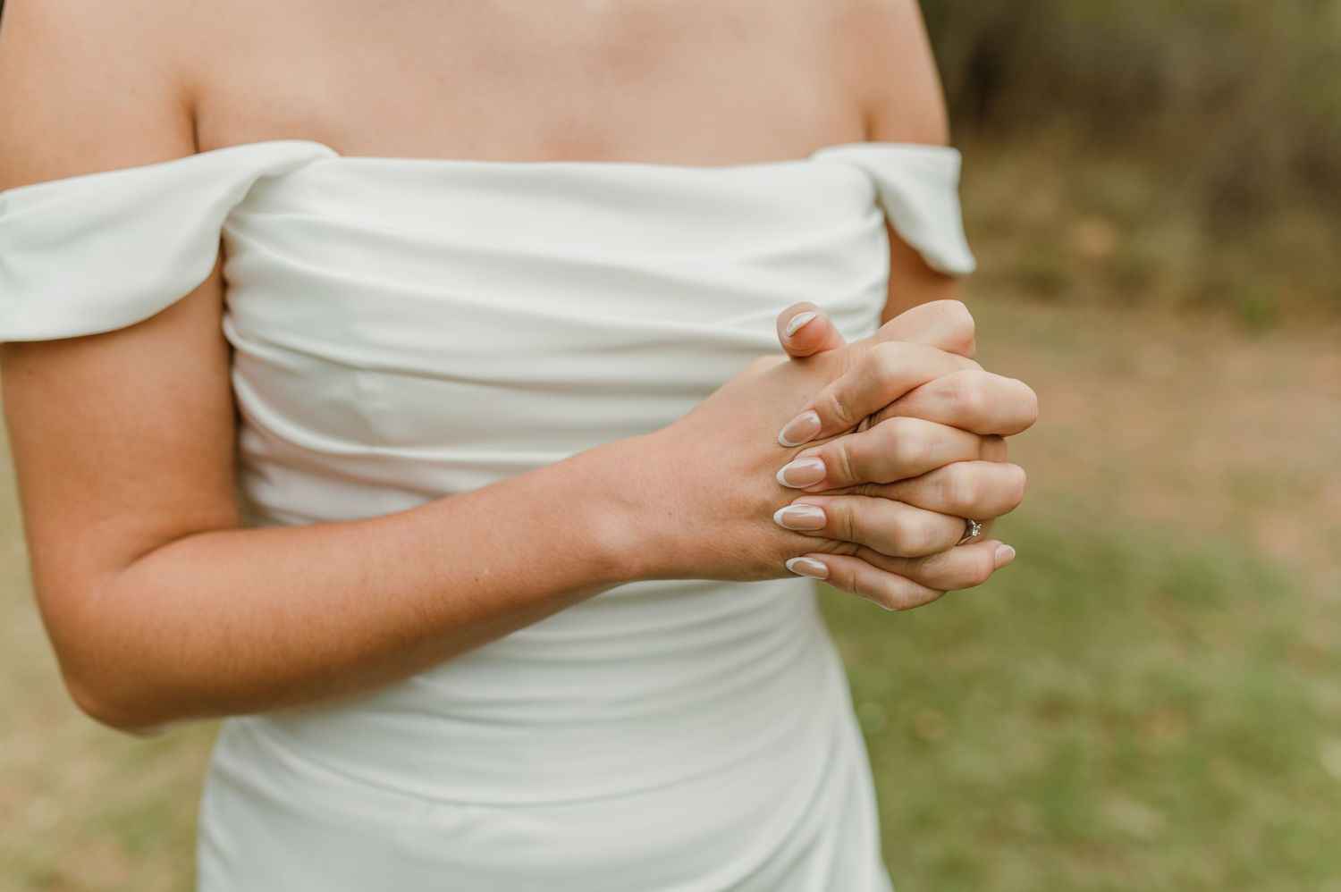 Detail shot of clasped hands showing wedding ring and off-shoulder white dress.