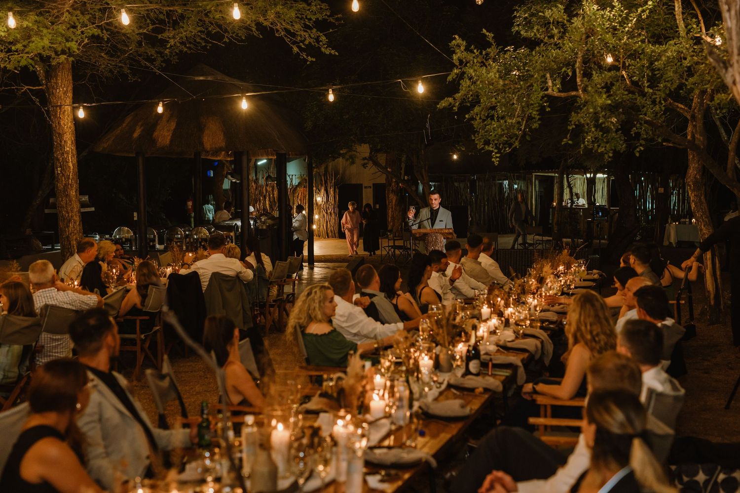 Long banquet tables set for an evening outdoor wedding reception with string lights overhead.