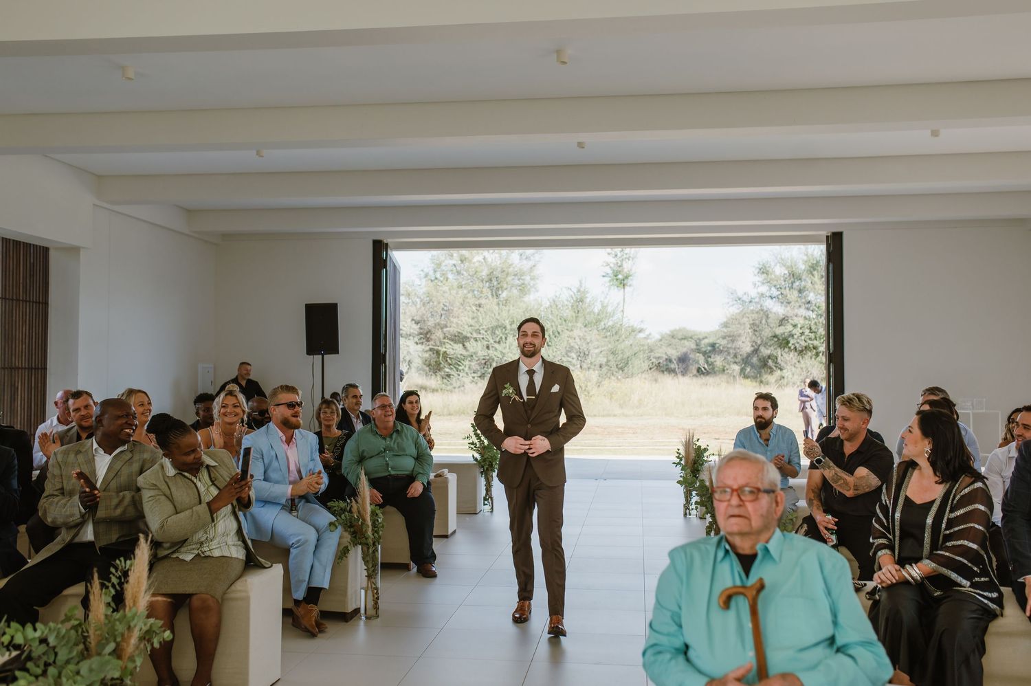 Wedding ceremony guests gathered in a bright modern space with white walls and large windows.