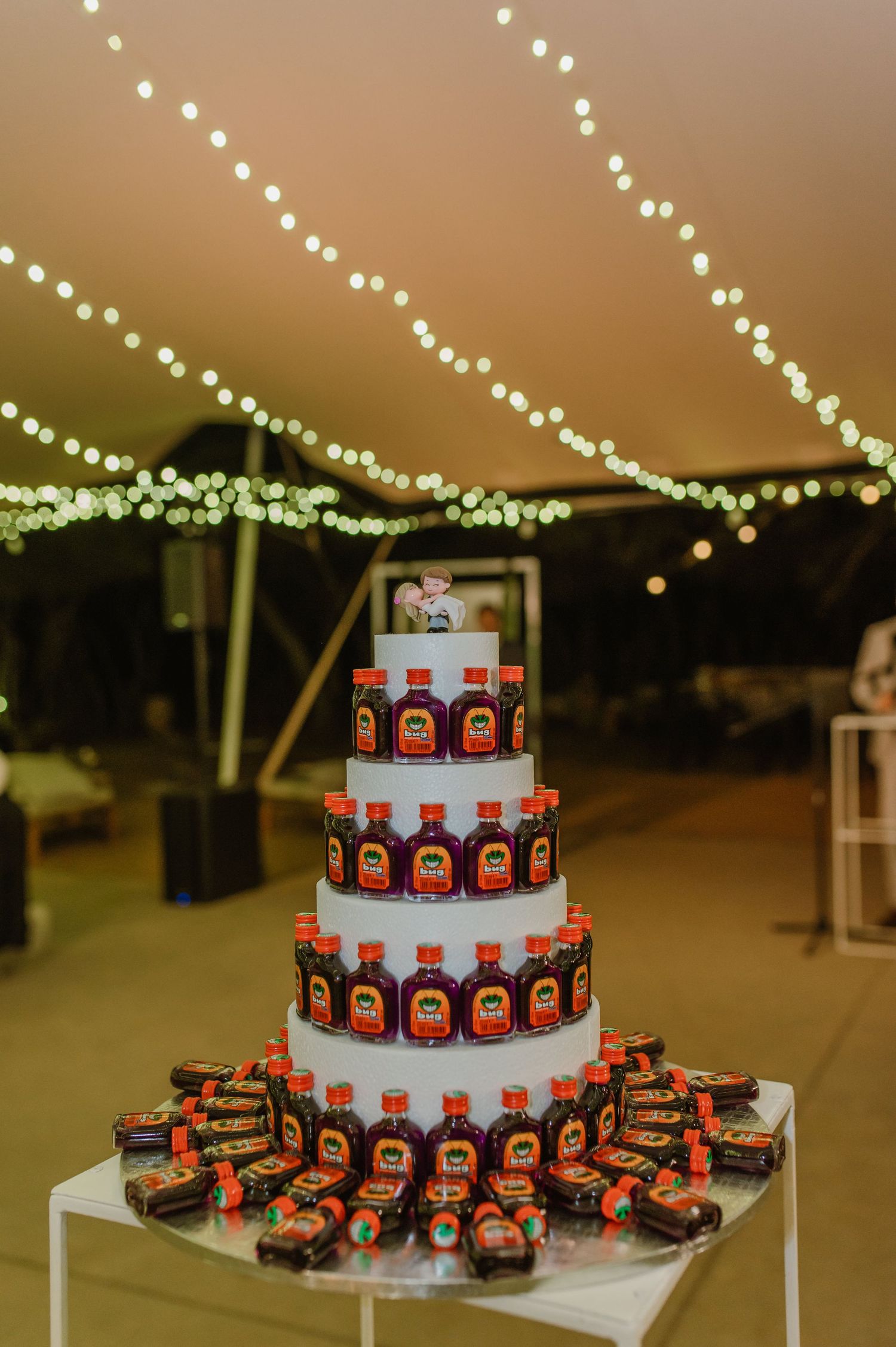 Unique tiered wedding cake display made entirely of Jagermeister bottles under string lights.