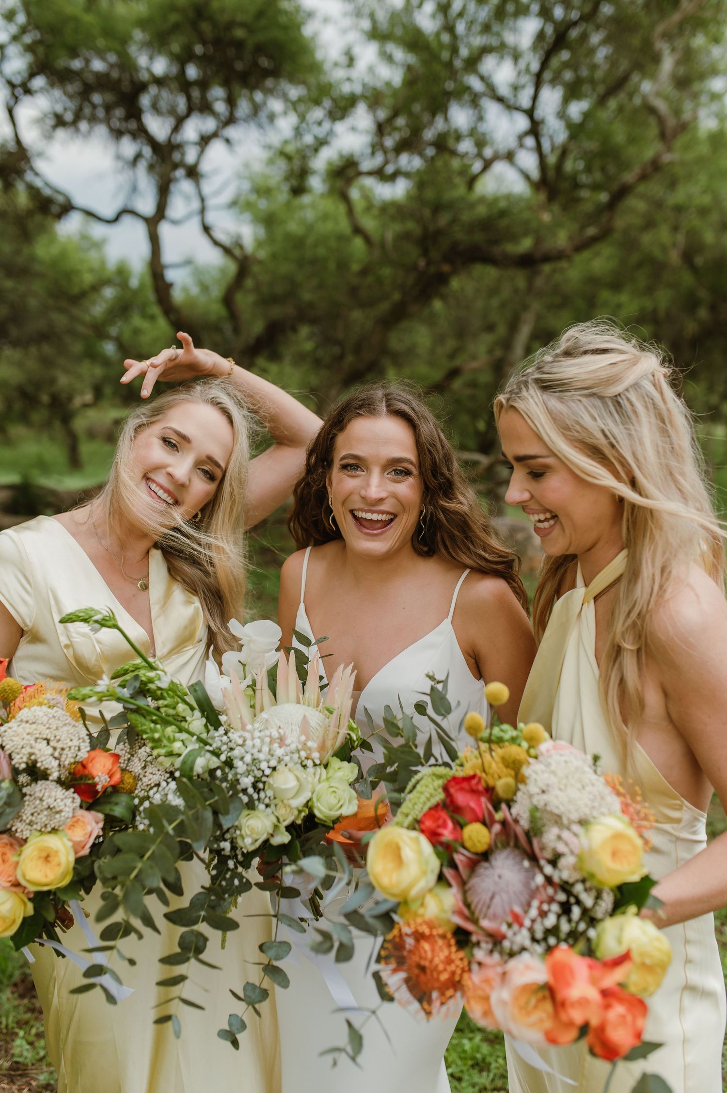 Bridesmaids in light dresses hold colorful bouquets while sharing candid laughter.