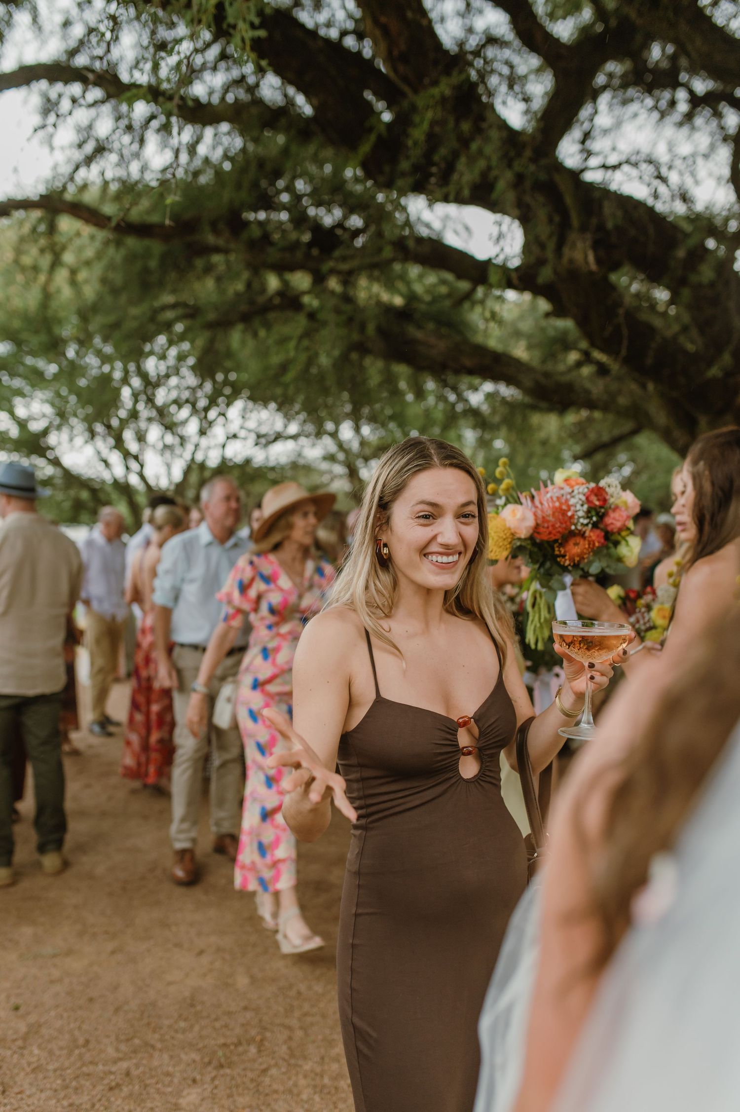 Wedding guests mingling under trees during an outdoor celebration.