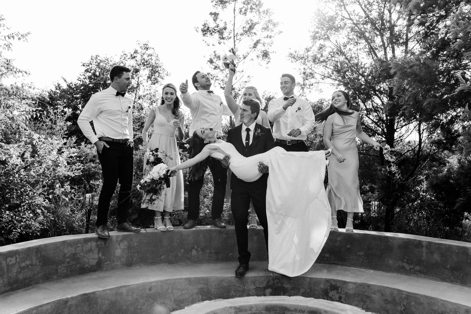 Black and white photo of wedding party jumping and celebrating outdoors.