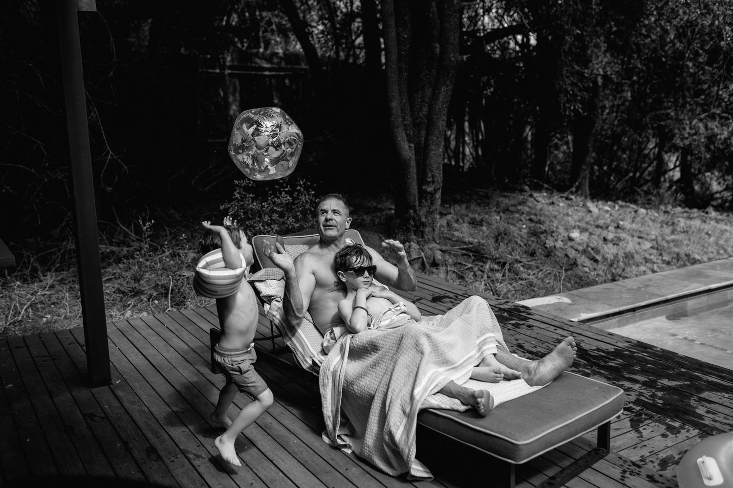 Couple relaxing on a lounge chair by a pool on a wooden deck in black and white photo.