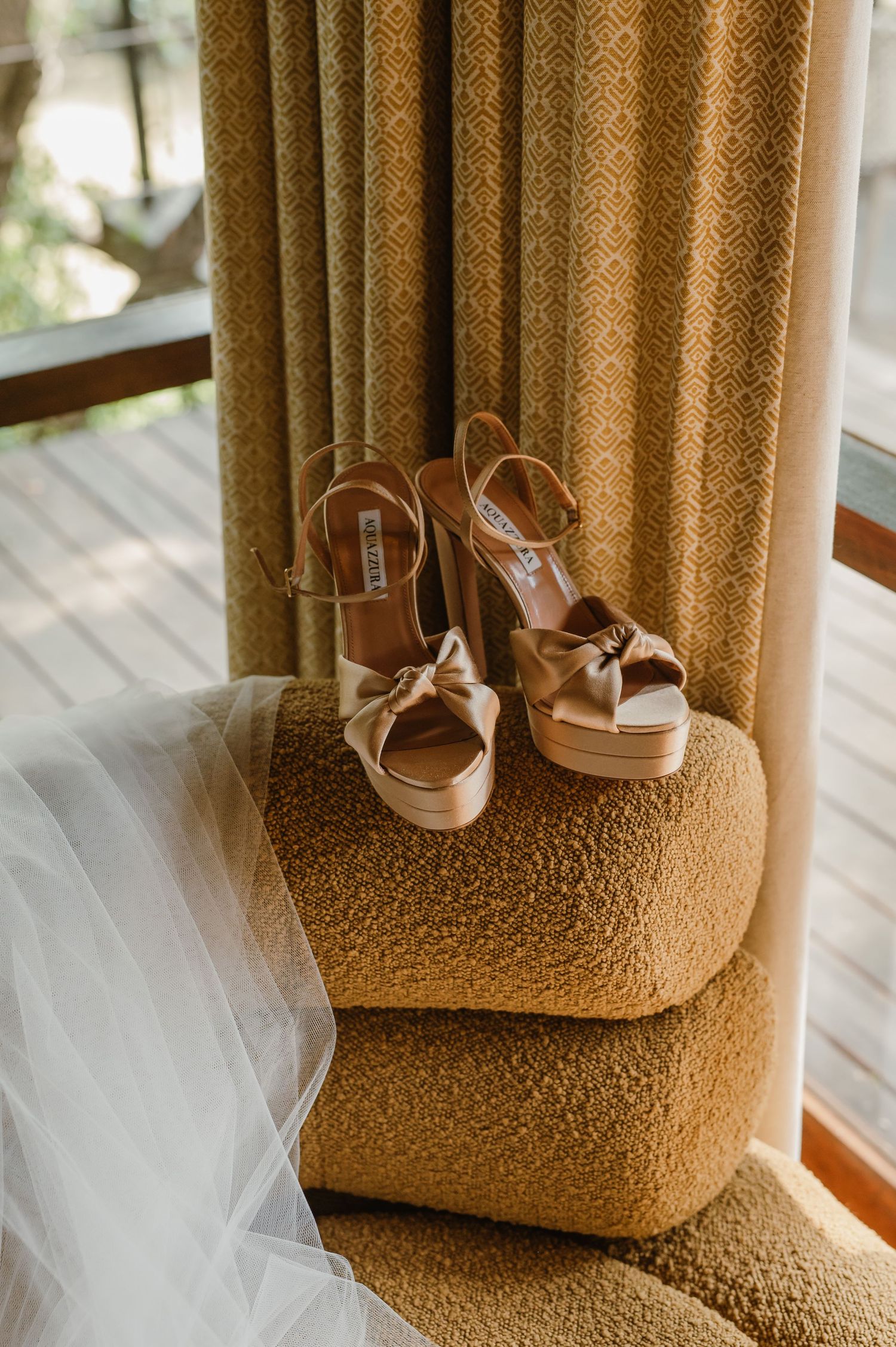 Nude satin Steve Madden platform heels with bow detail resting on textured gold ottoman beside bridal veil.