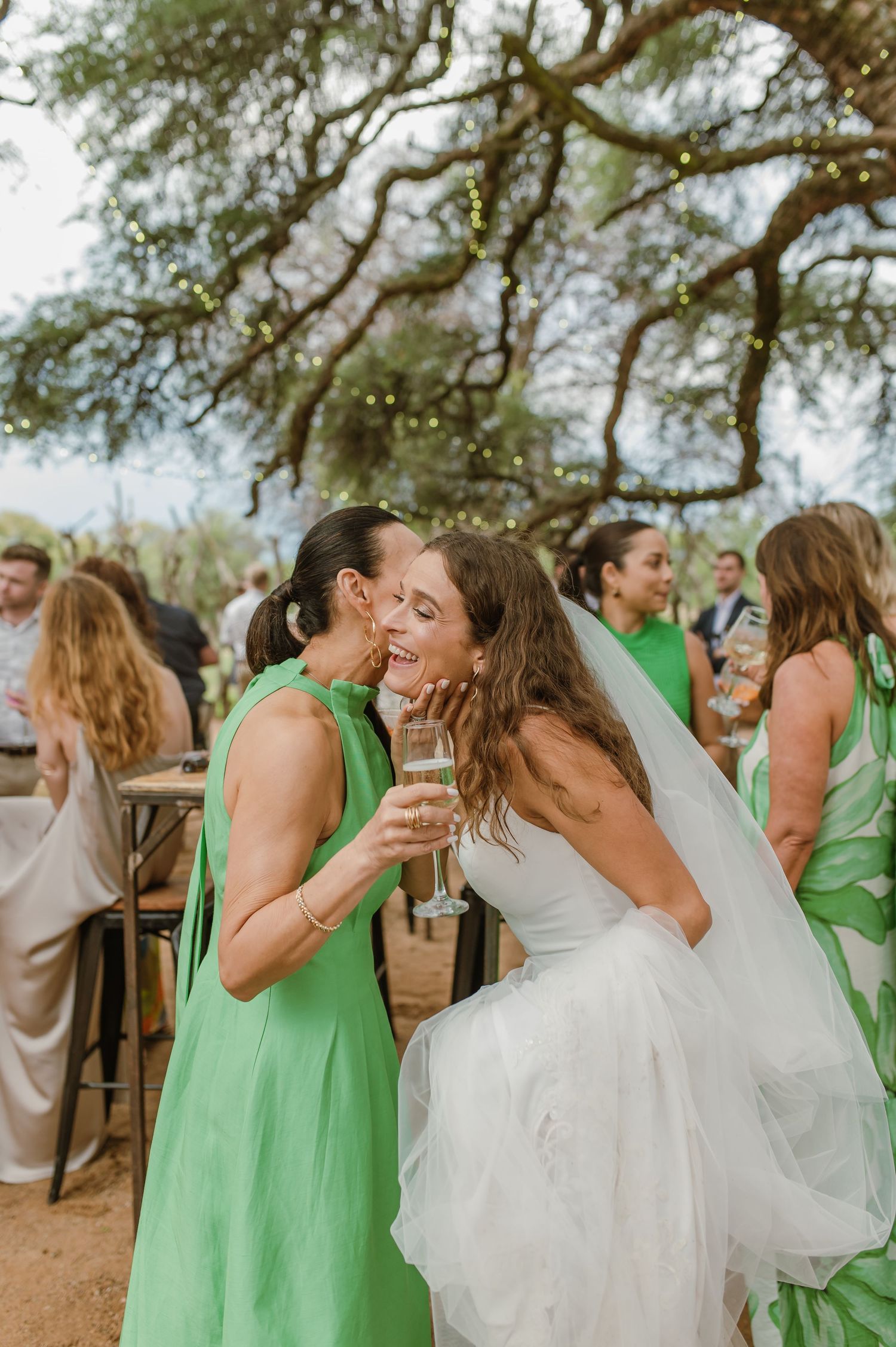 Wedding party in white and green dresses celebrating with champagne outdoors.