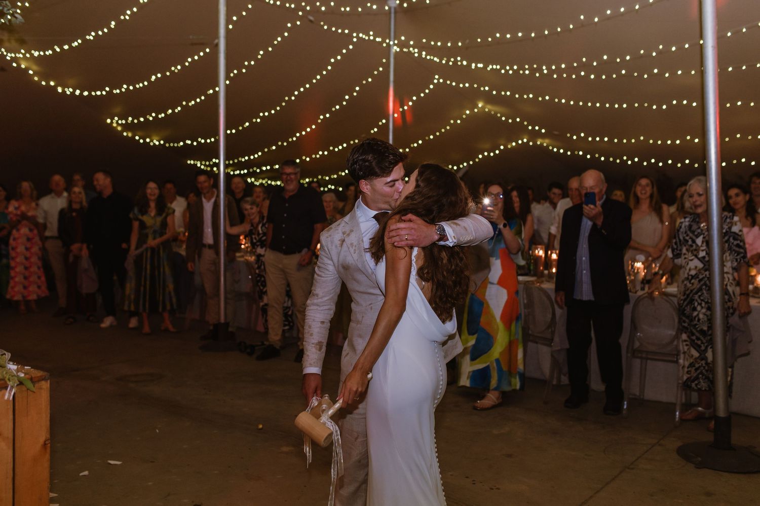 Wedding guests dance and celebrate on a festive dance floor under twinkling string lights.