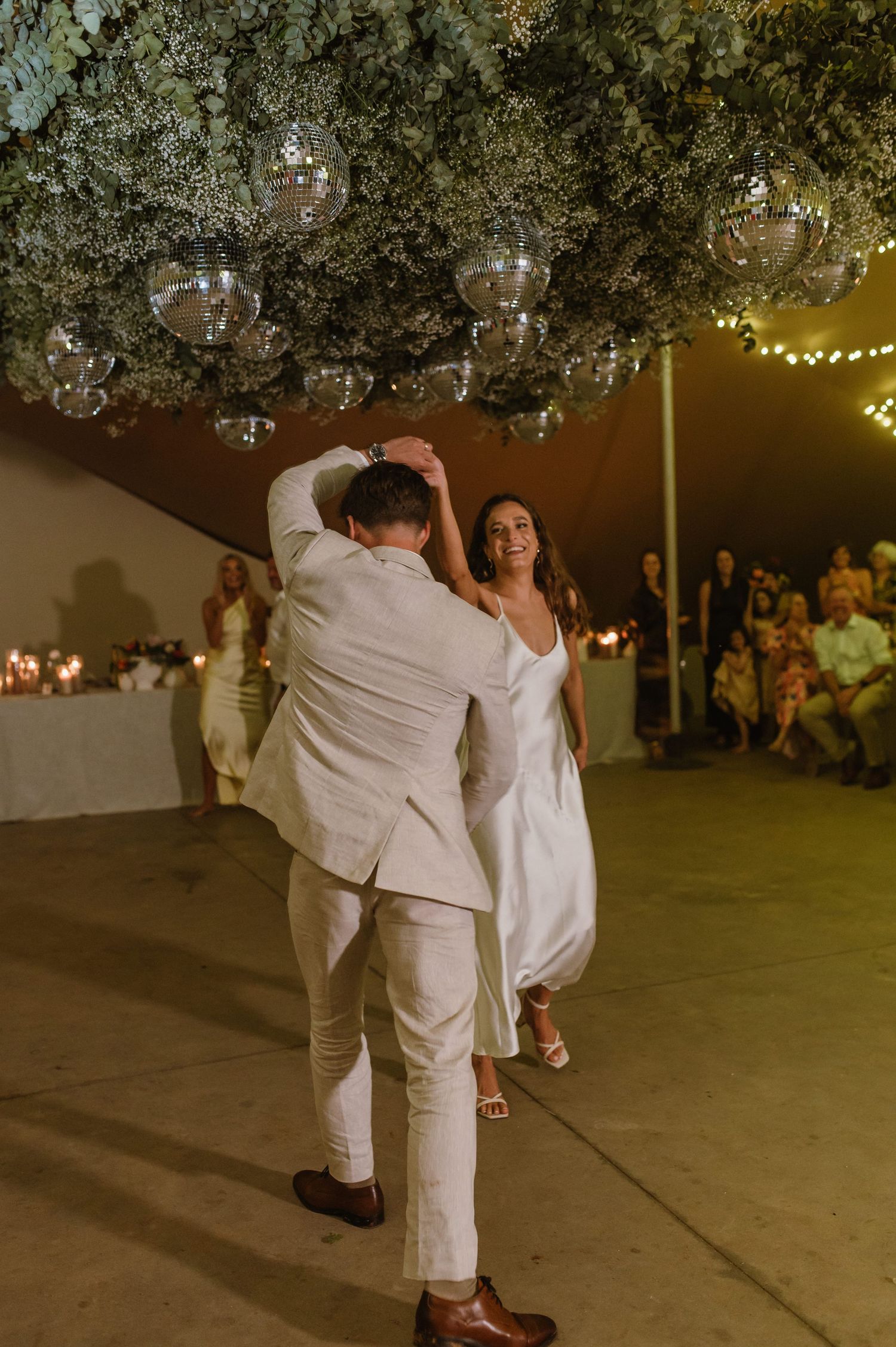 A romantic dance move during the first dance at a wedding reception with string lights overhead.