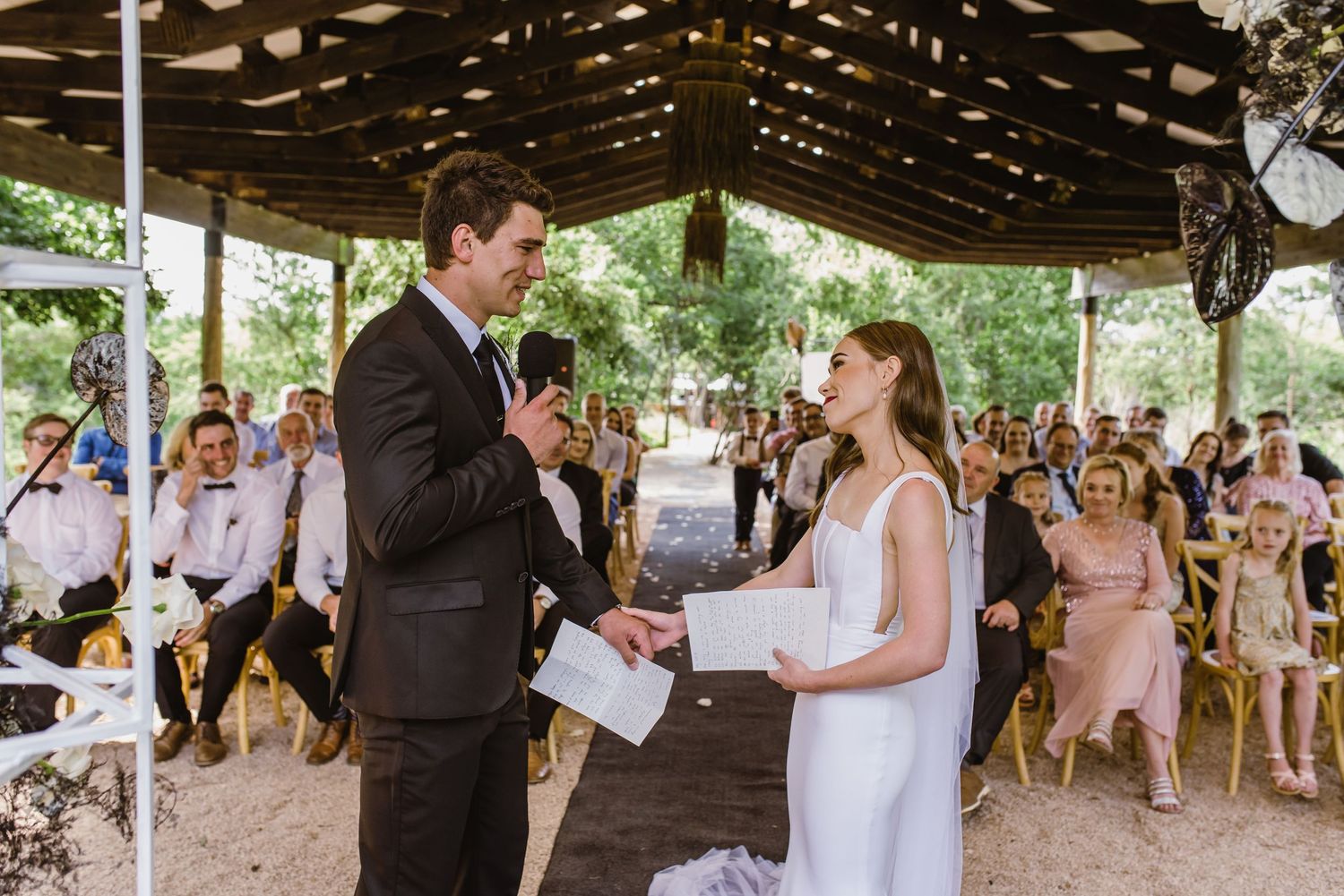 Wedding ceremony taking place under a wooden pavilion surrounded by natural greenery.