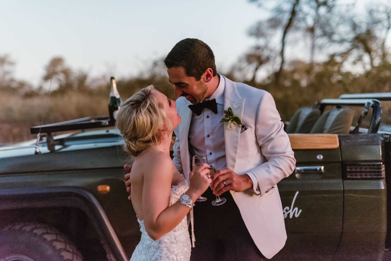 Couple shares intimate moments next to classic Land Rover vehicles during sunset wedding photography.