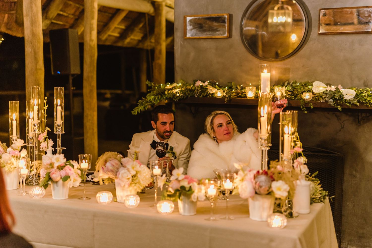 Rustic wedding venue with wooden beams and elegant table settings illuminated by candlelight.