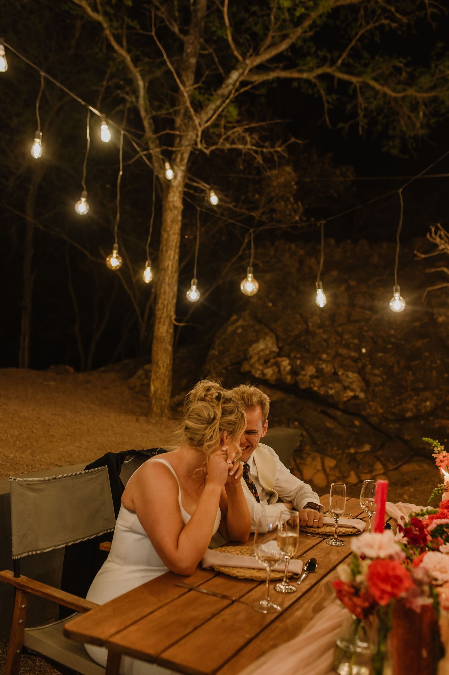 Intimate dinner party scene with warm lighting and red floral centerpieces on wooden tables.