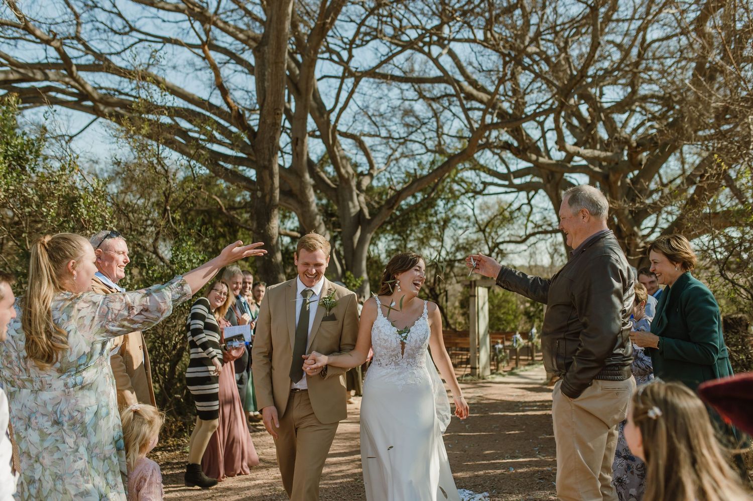 Wedding party gathered in a rustic outdoor setting with natural tree canopy overhead.