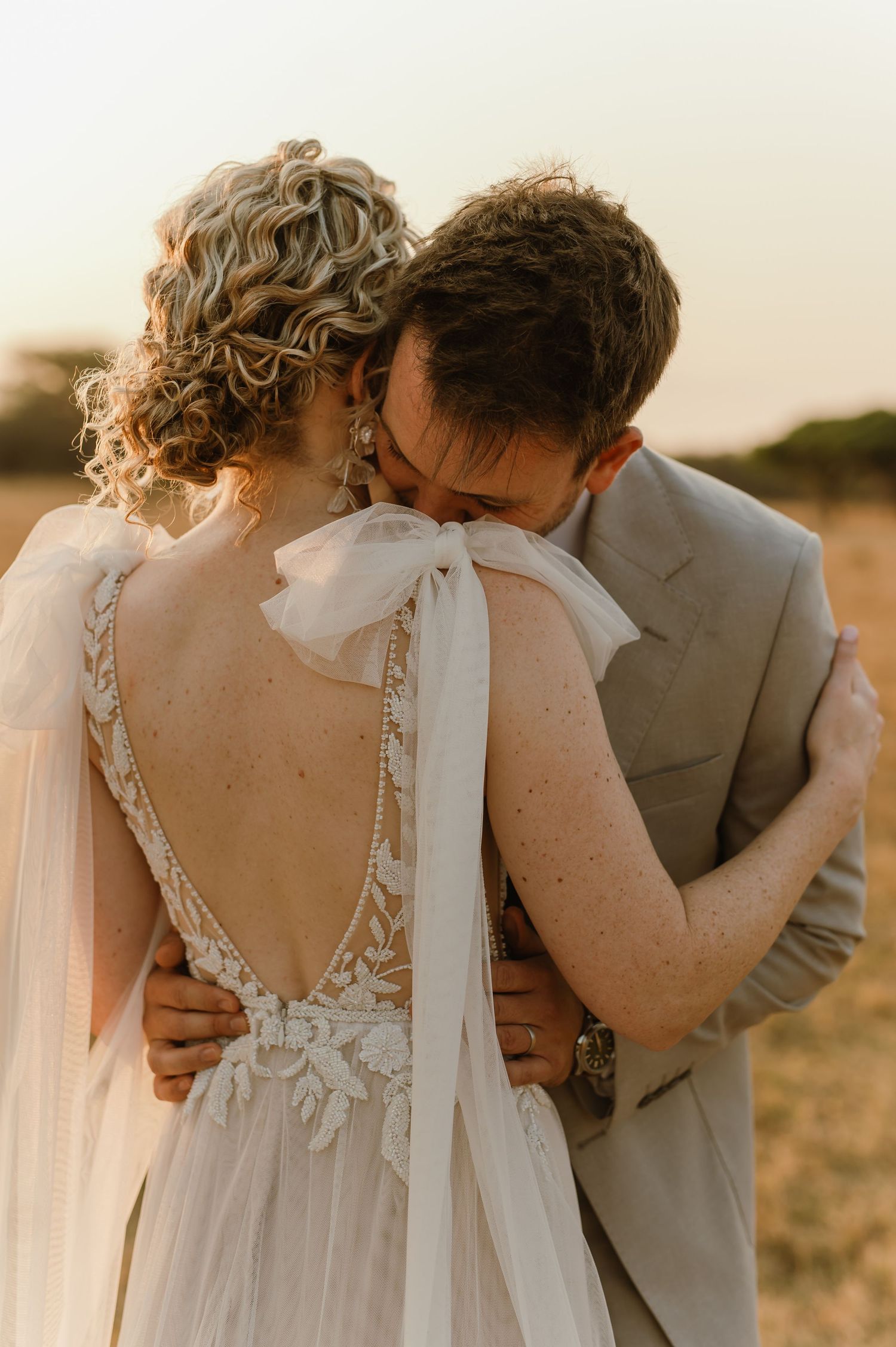 Close-up of bride's detailed lace back wedding dress with bow during intimate moment.