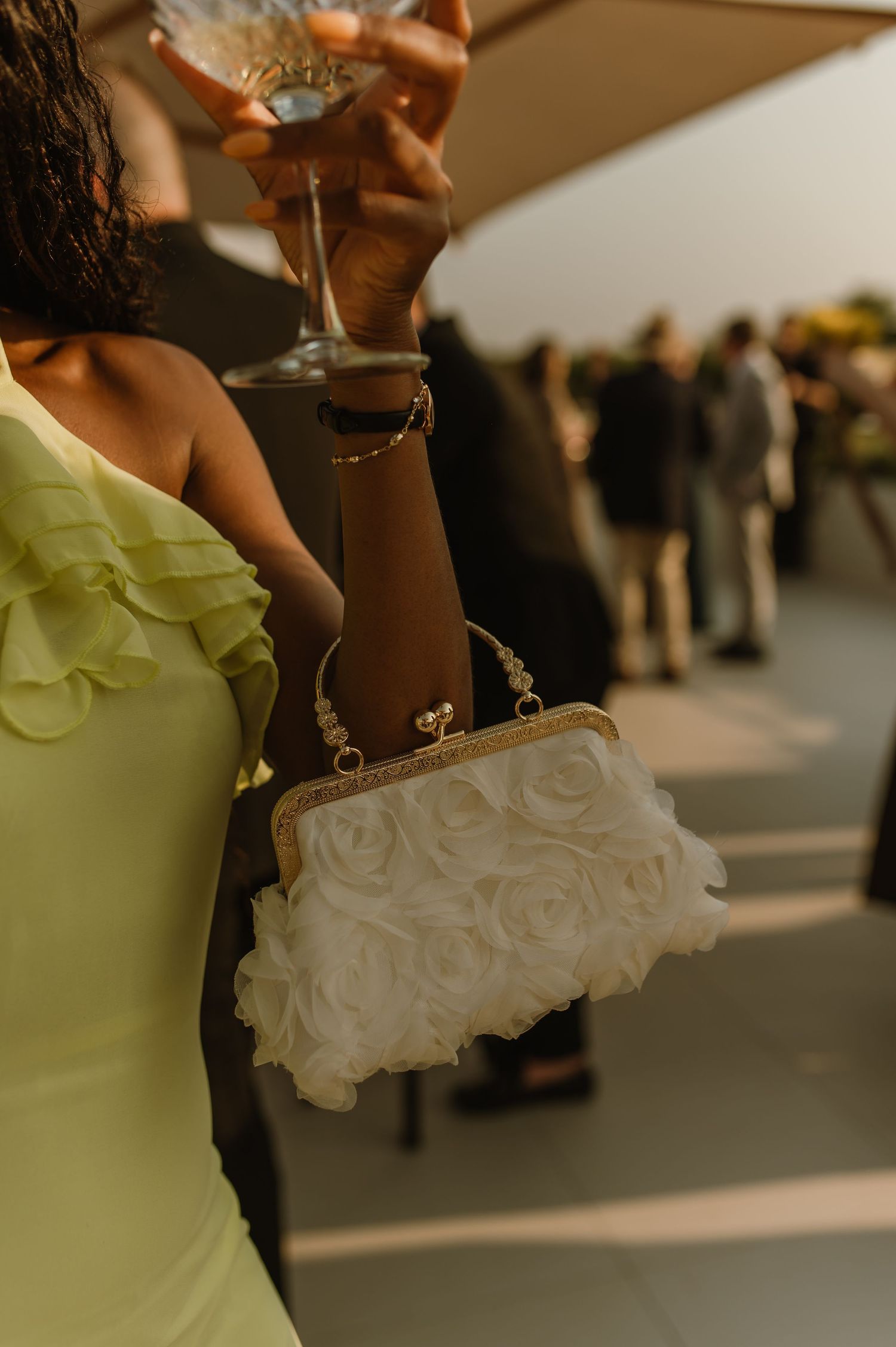 Person in a light green dress holding a champagne glass at an outdoor event.