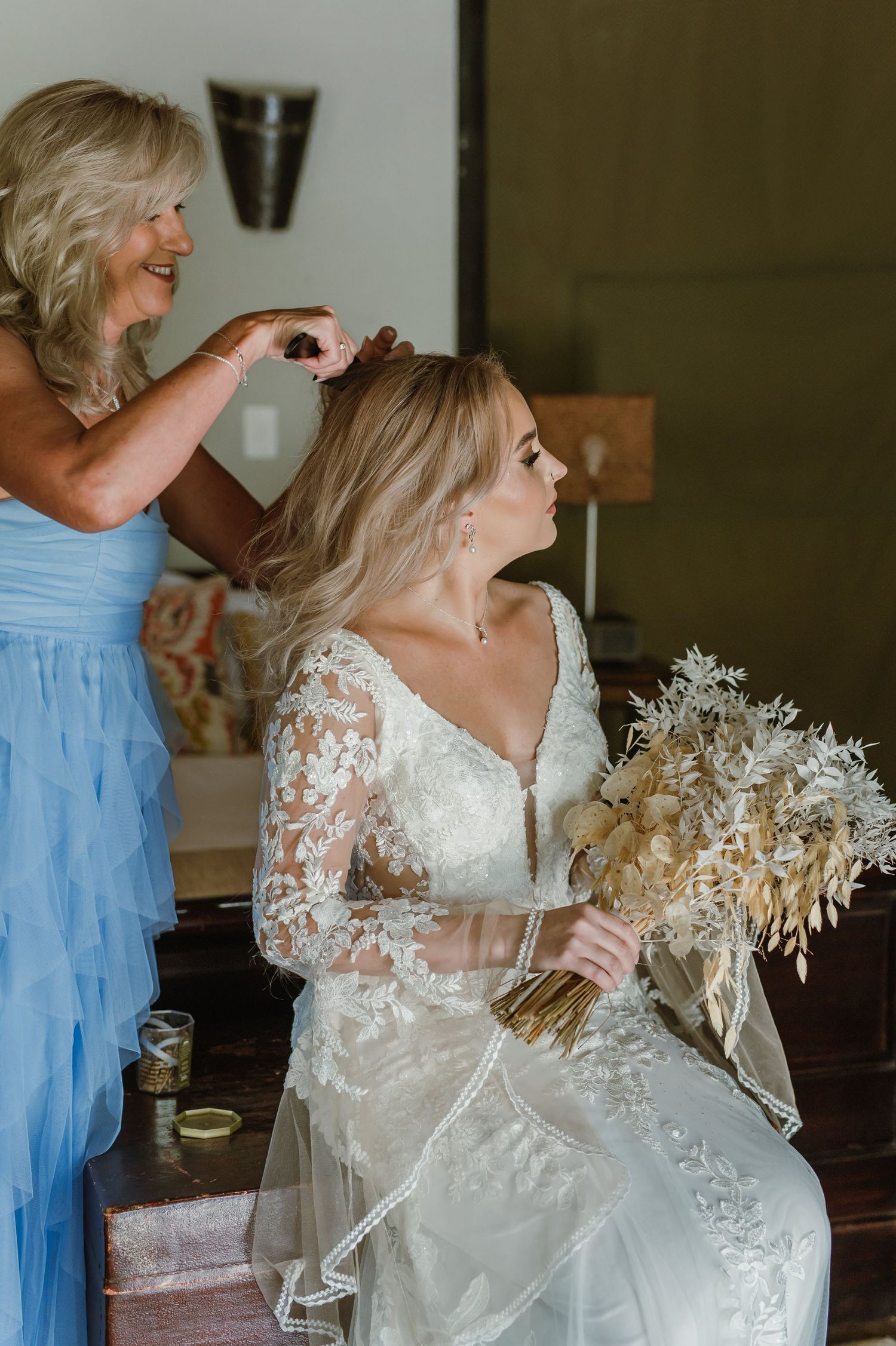 Final wedding preparations with dried floral bouquet and elegant lace gown details.