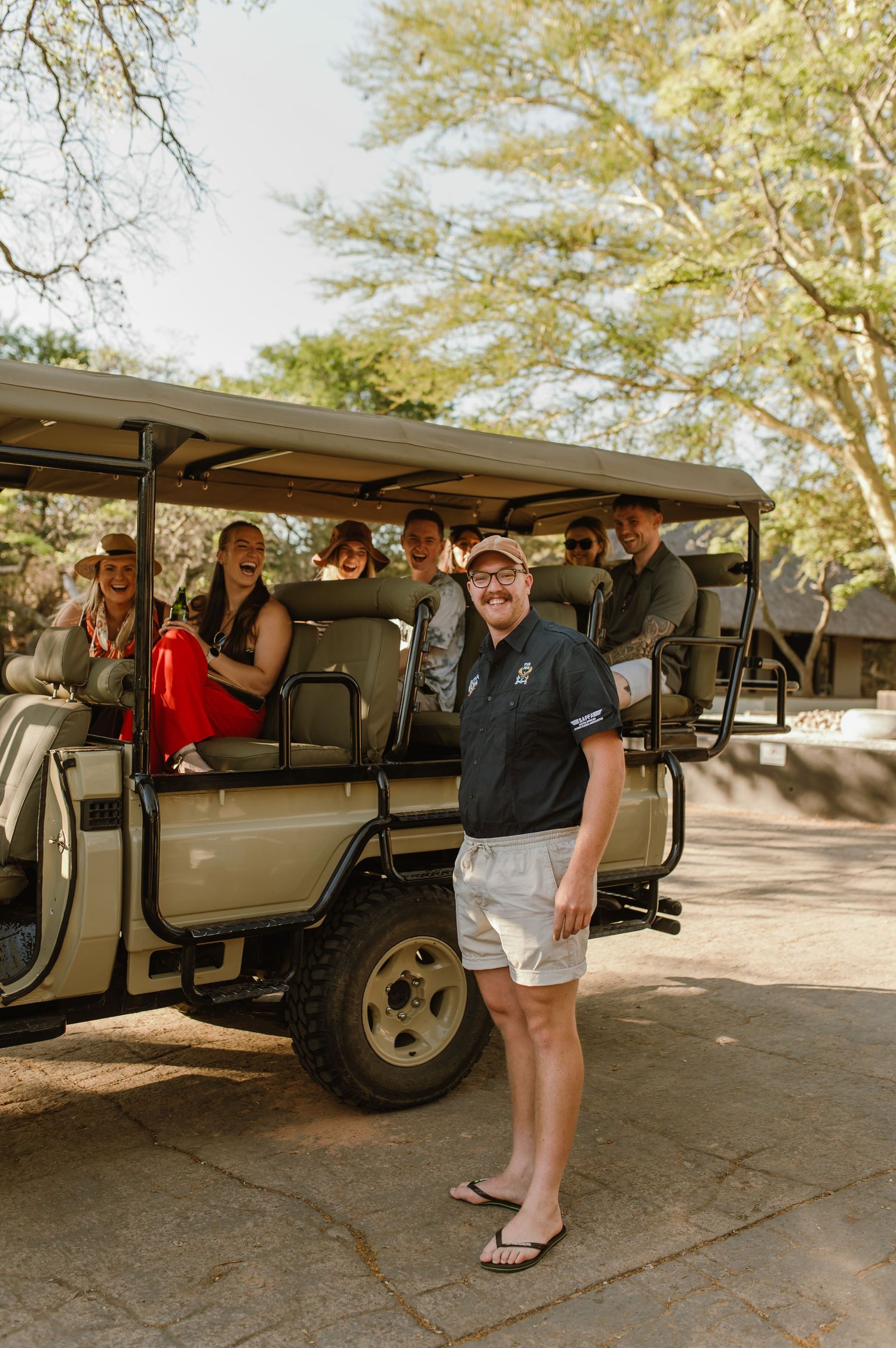 Safari vehicles parked in sequence on dirt ground under trees.