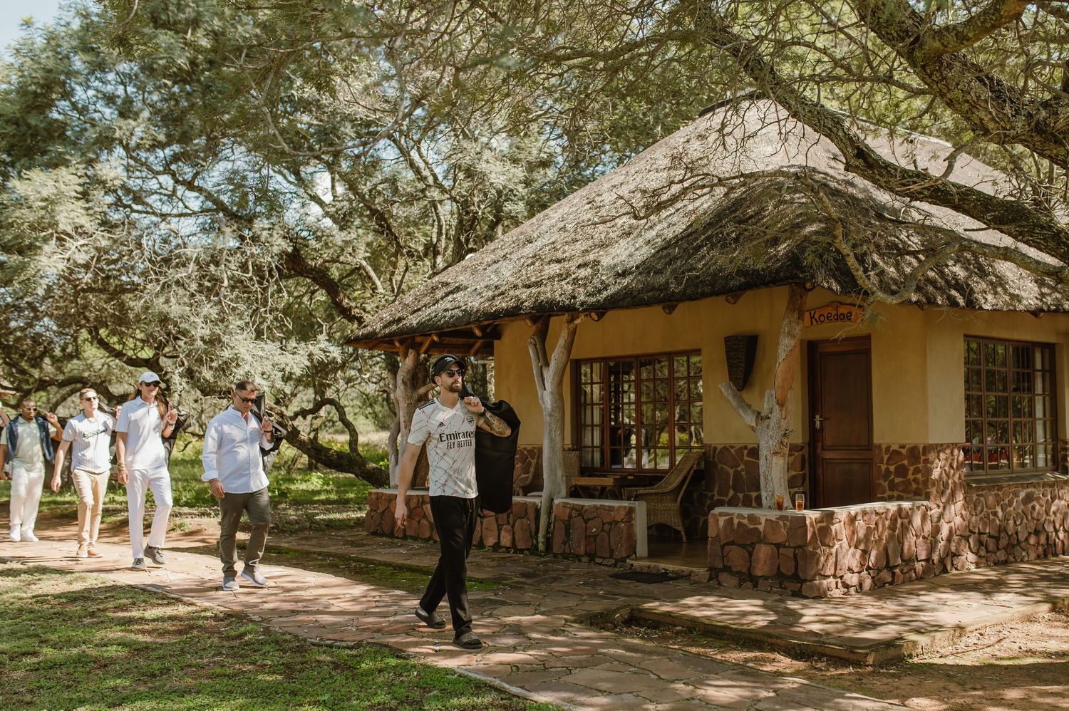 Traditional African lodge buildings with thatched roofs nestled among shady trees.