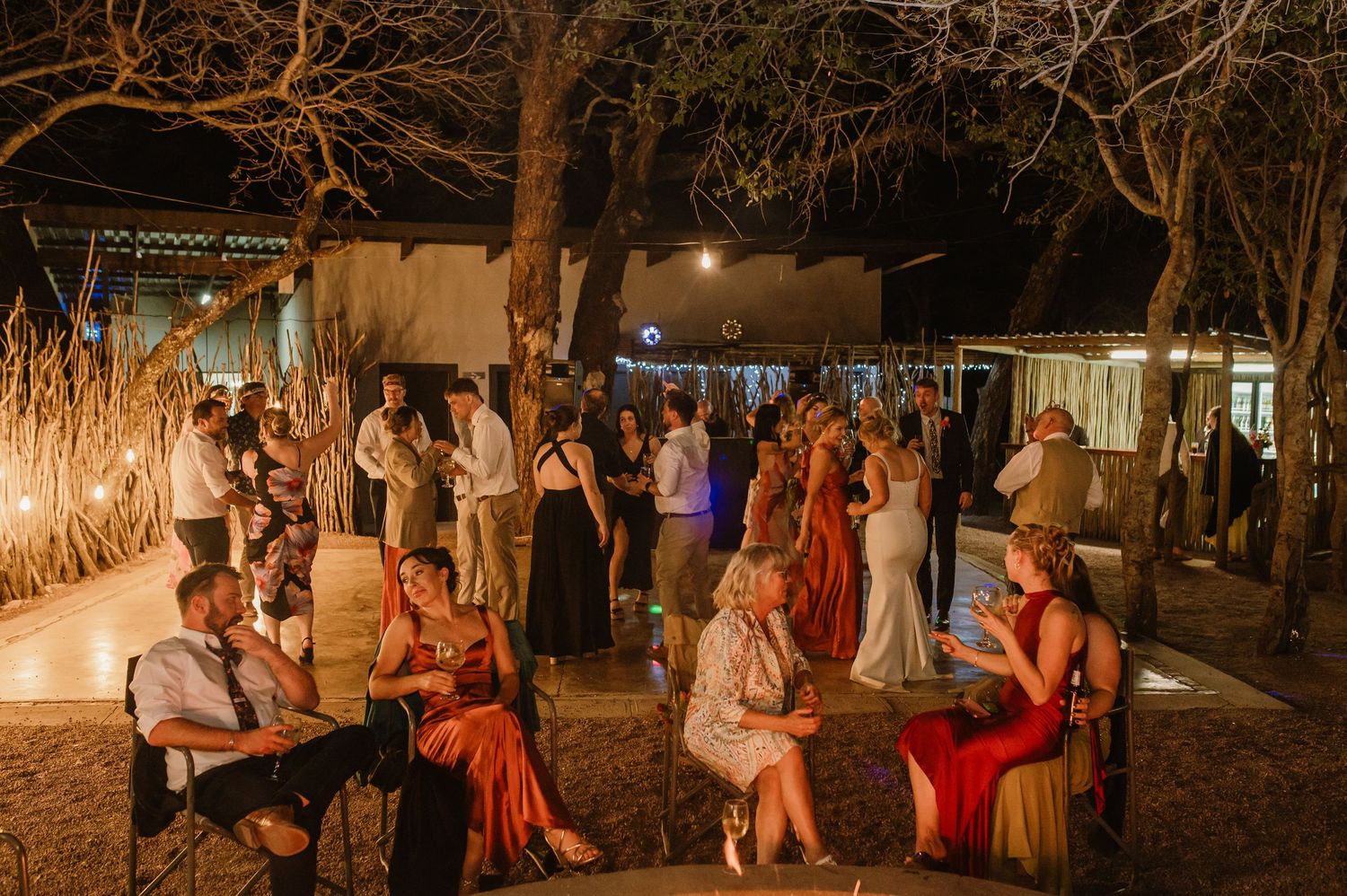 Evening wedding reception with guests relaxing at outdoor venue under ambient lighting.