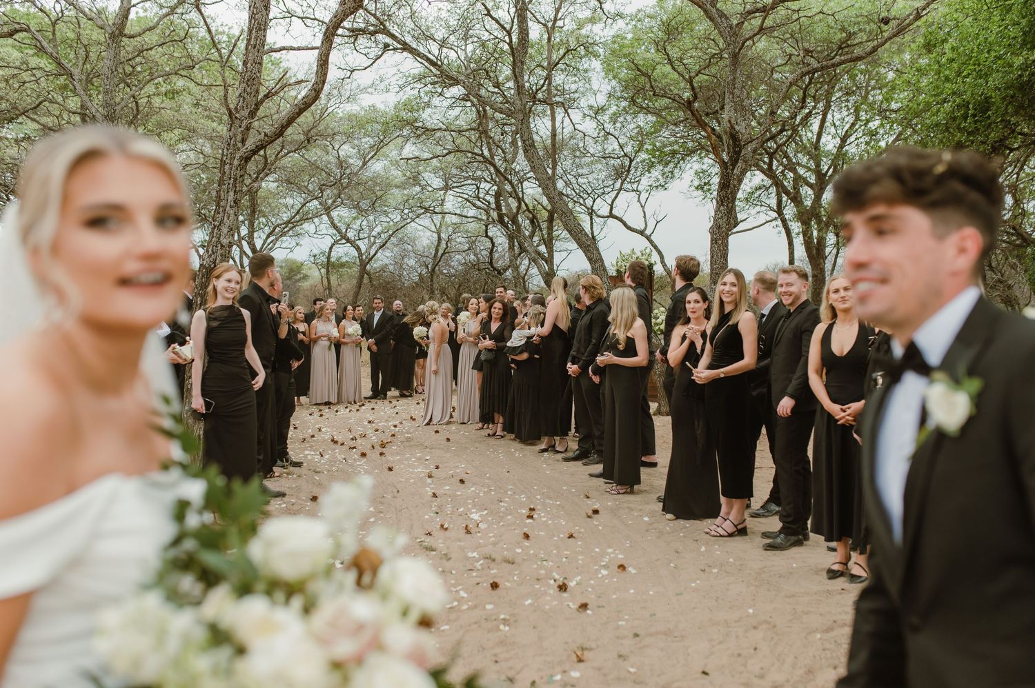 Wedding celebration on rustic path with guests lined up in black formal wear.