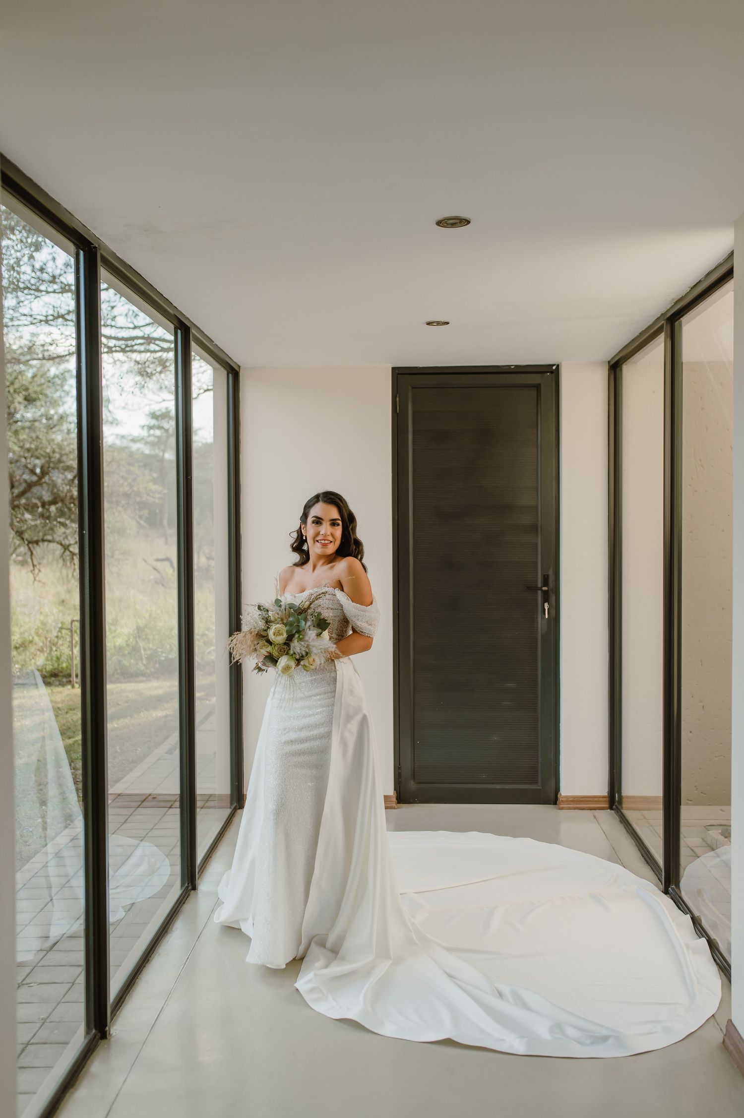 Elegant white wedding dress flowing in a modern room with floor-to-ceiling windows and natural light.