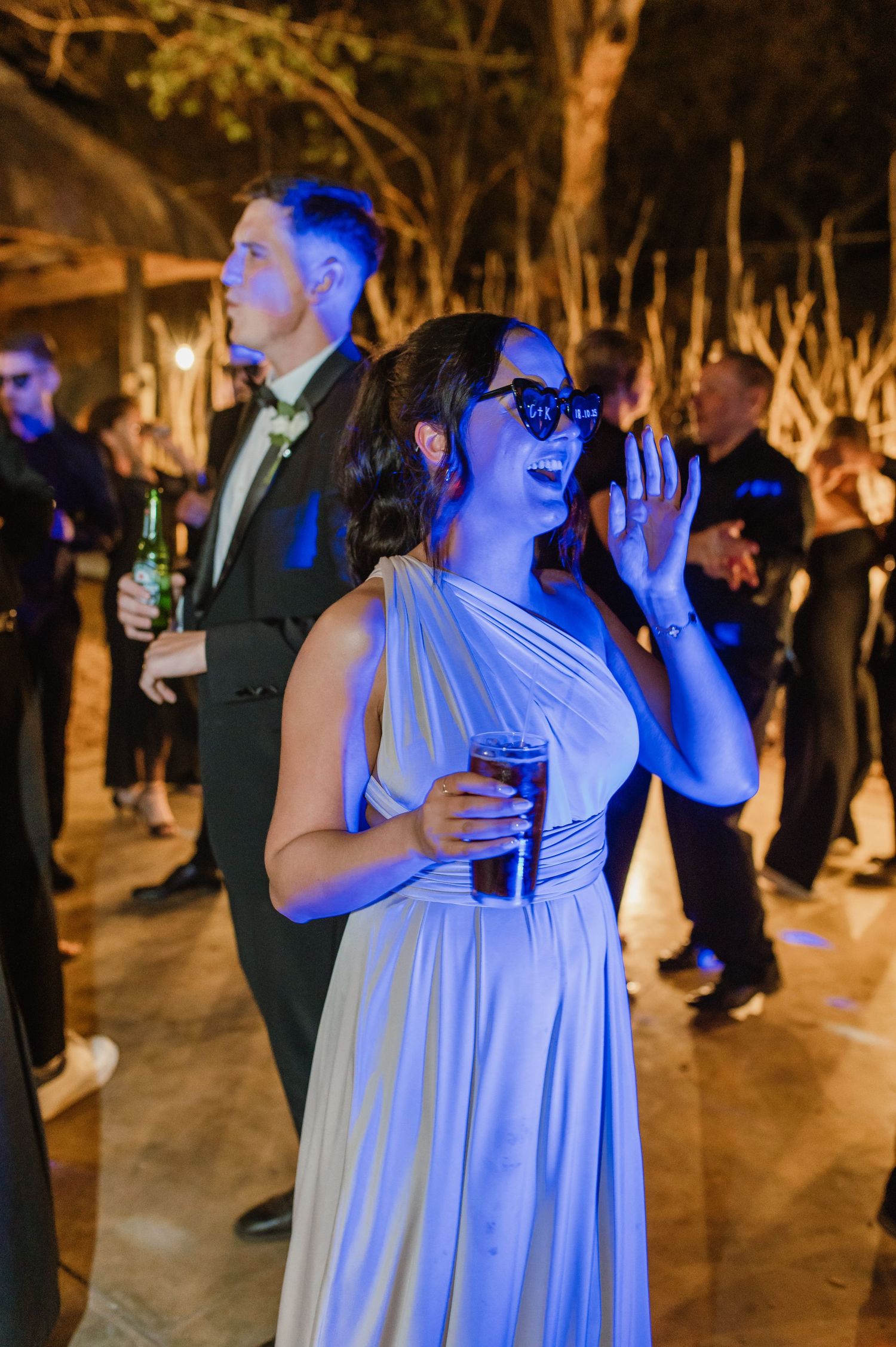 Party guests celebrate under blue lighting at an evening outdoor venue.
