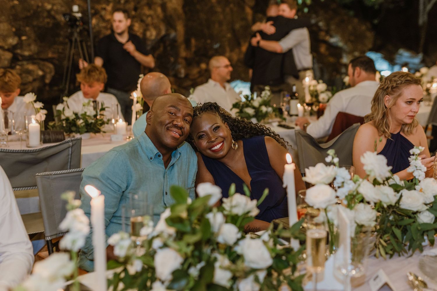 Wedding reception tables adorned with white floral centerpieces and glowing candles in an outdoor setting.