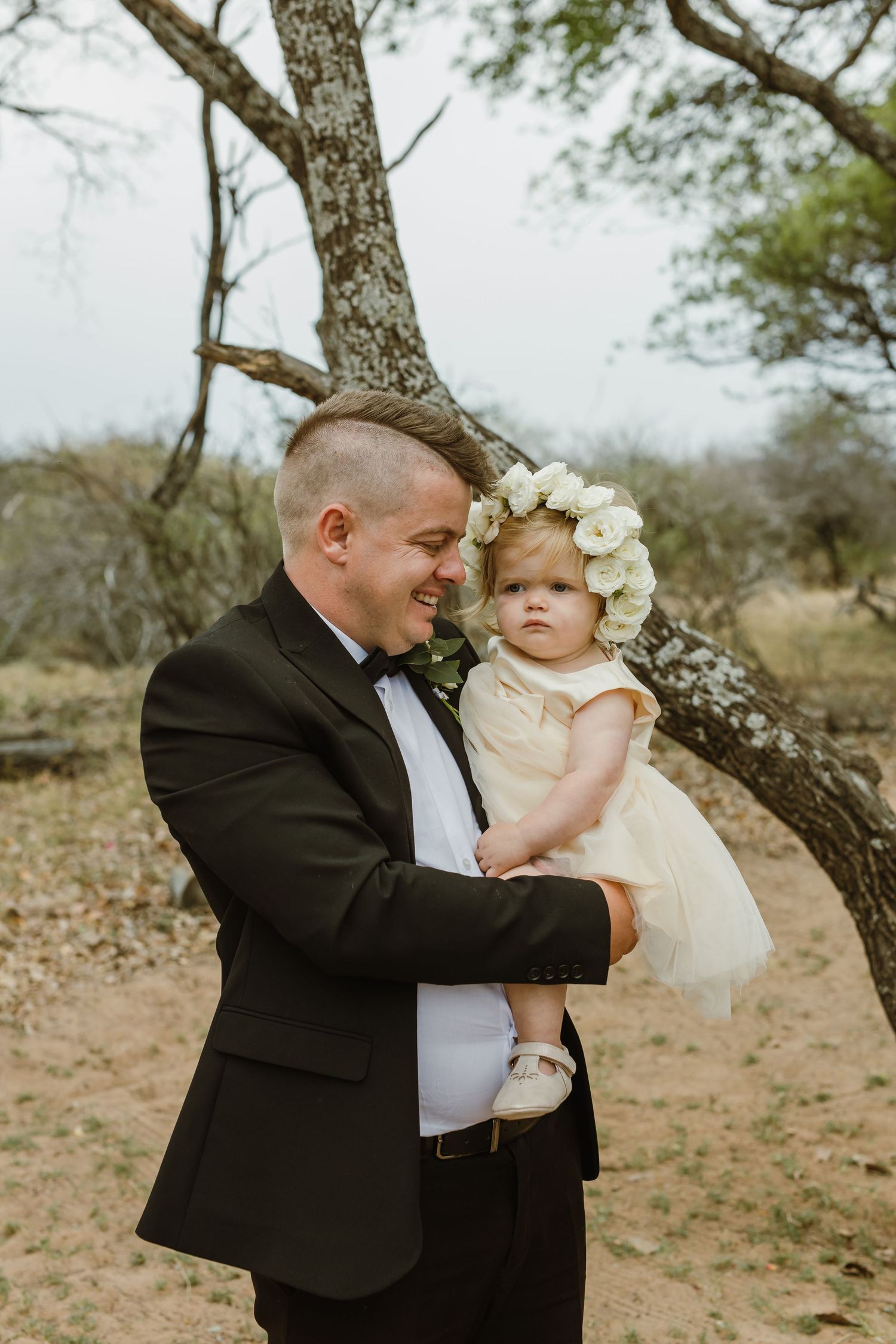 Sweet moment between adult and baby in formal attire under a tree.