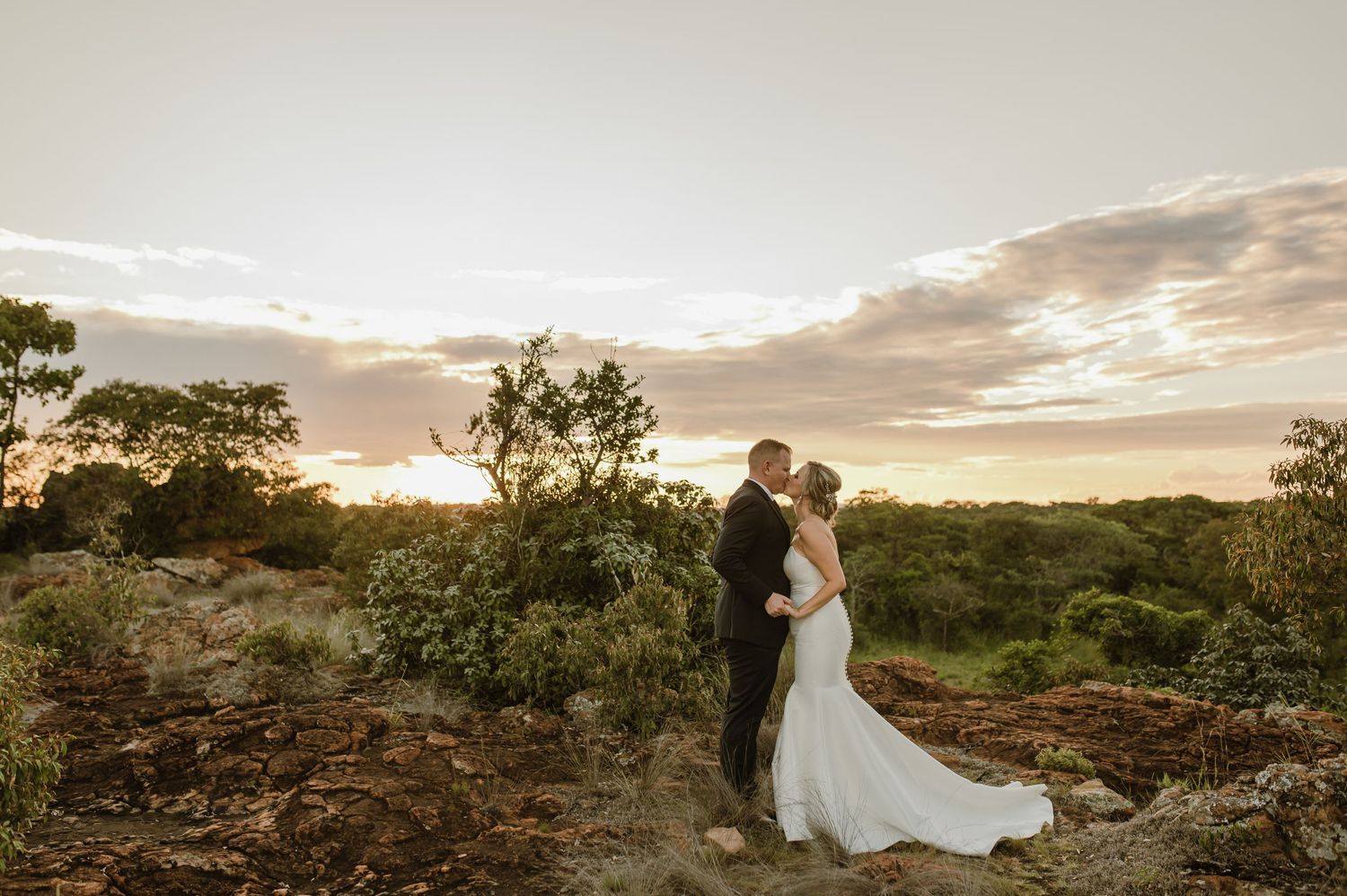 Panoramic wedding photo captures couple against dramatic sunset sky and desert landscape.