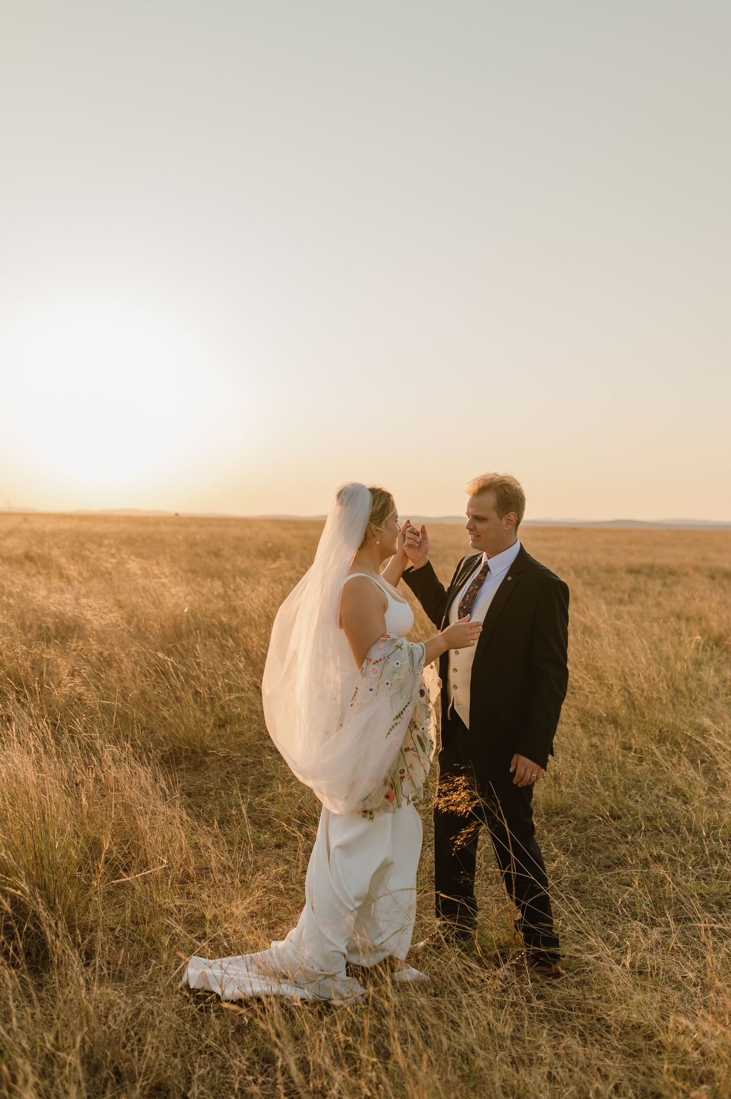 Wedding couple sharing intimate moment in grassy field at golden hour.