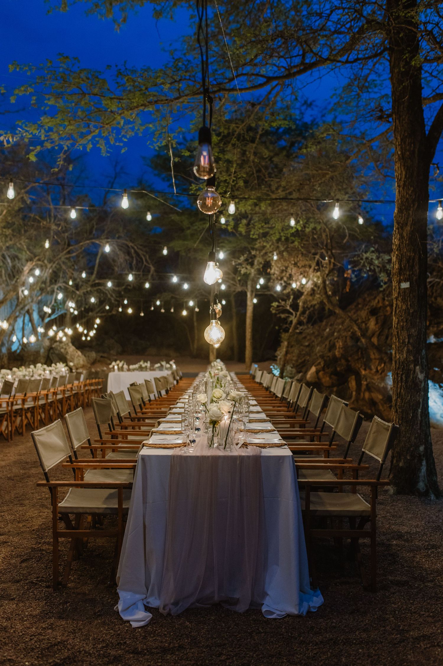 Long banquet tables arranged under string lights for an outdoor evening wedding reception.