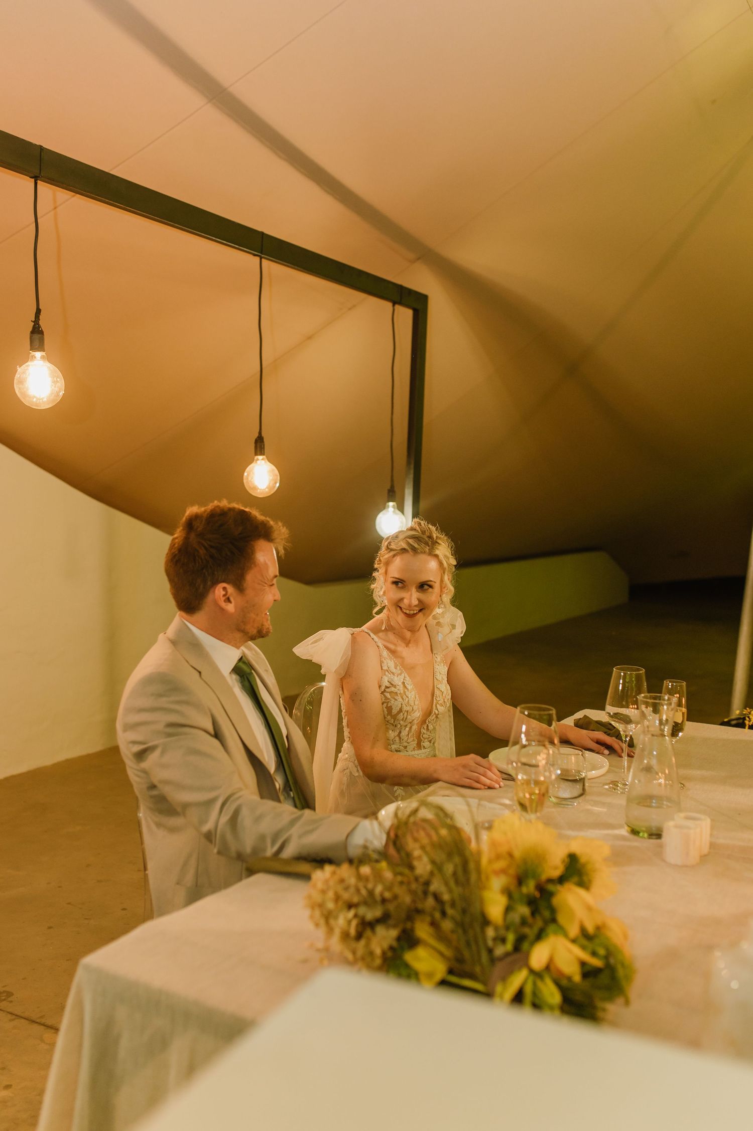 Couple shares an intimate moment at their reception table under pendant lights.