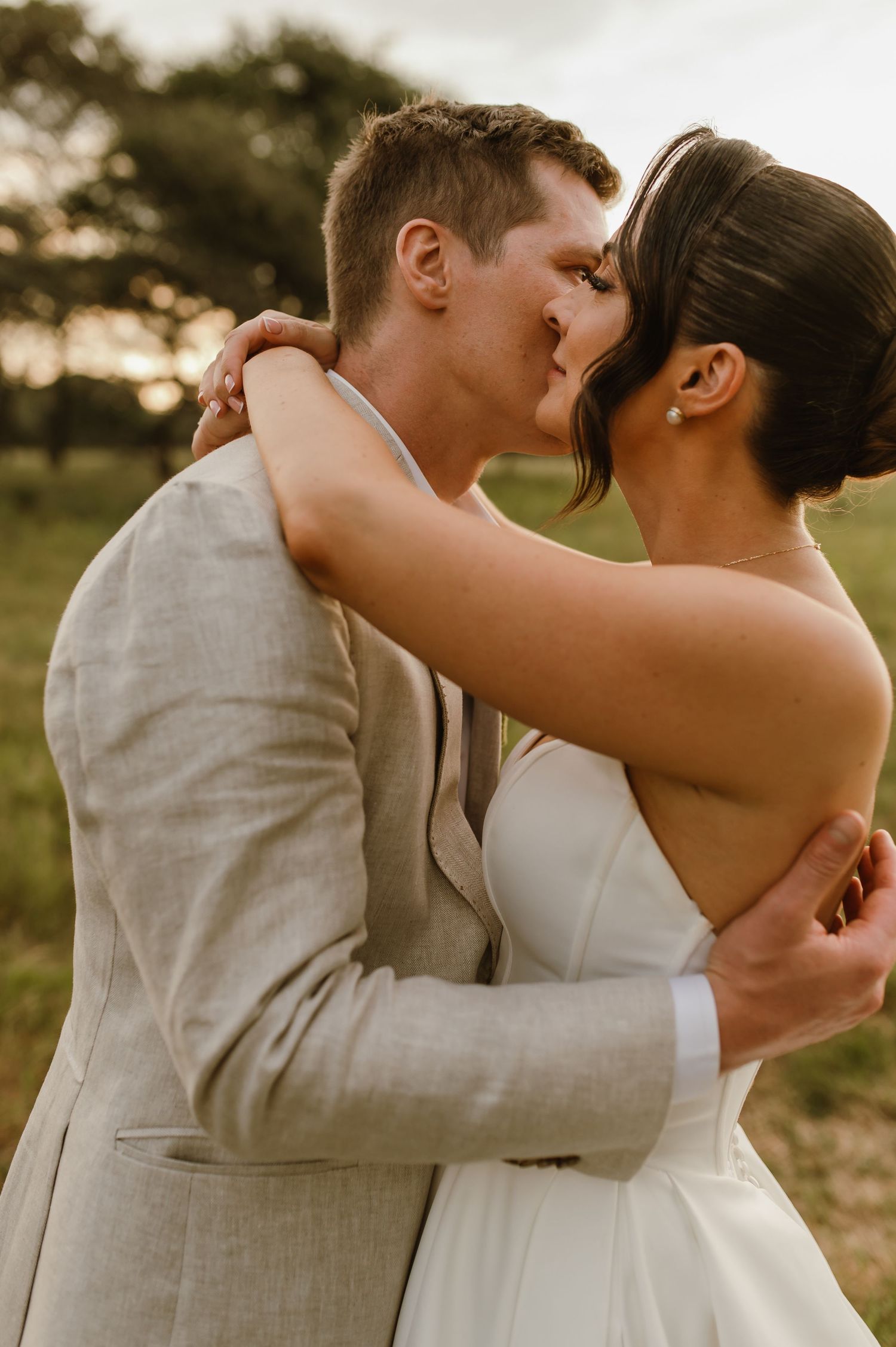 A romantic embrace between newlyweds in white and light gray attire during their outdoor photoshoot.