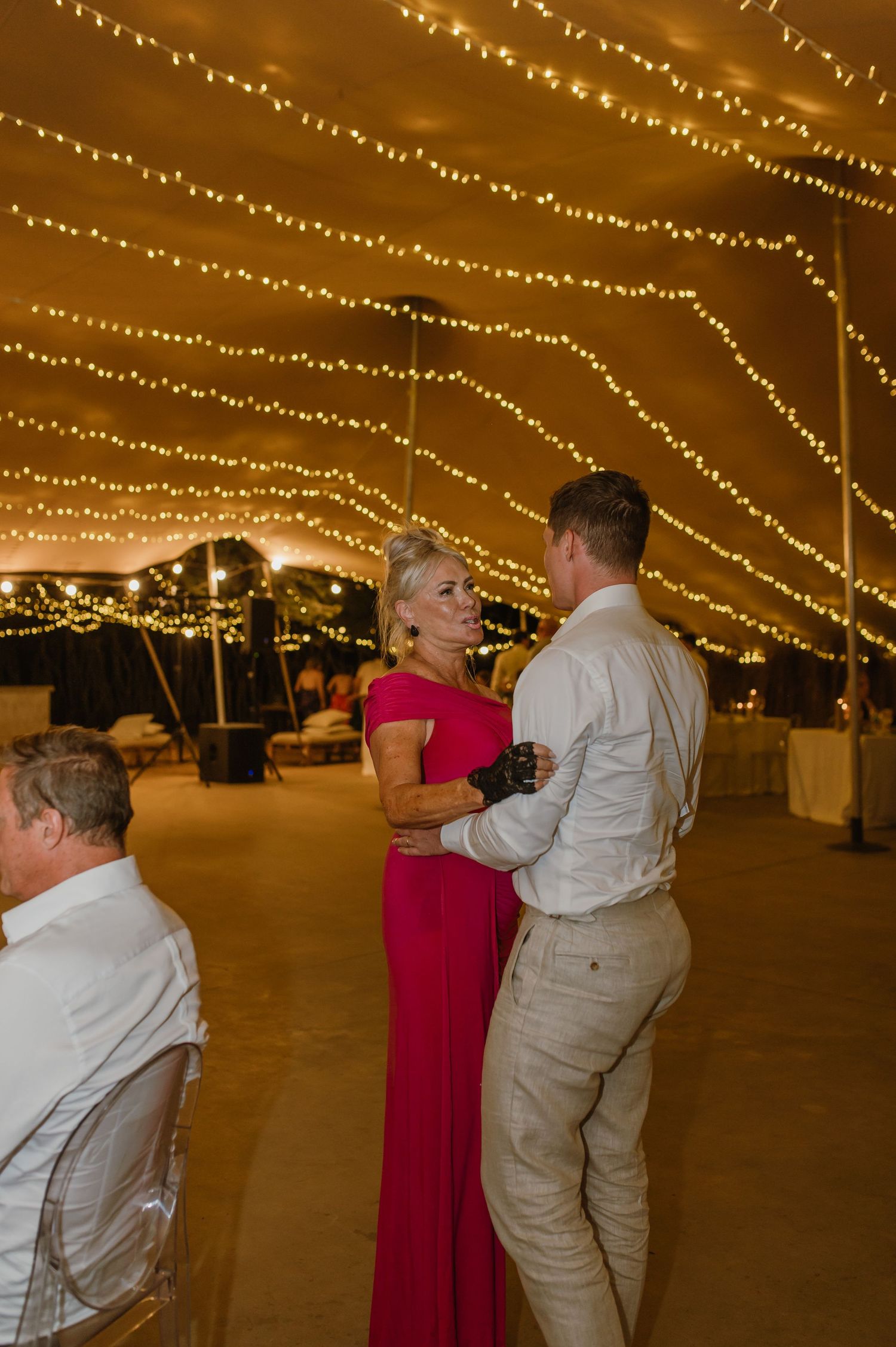 Couples dancing together under romantic string light canopy at evening wedding reception.