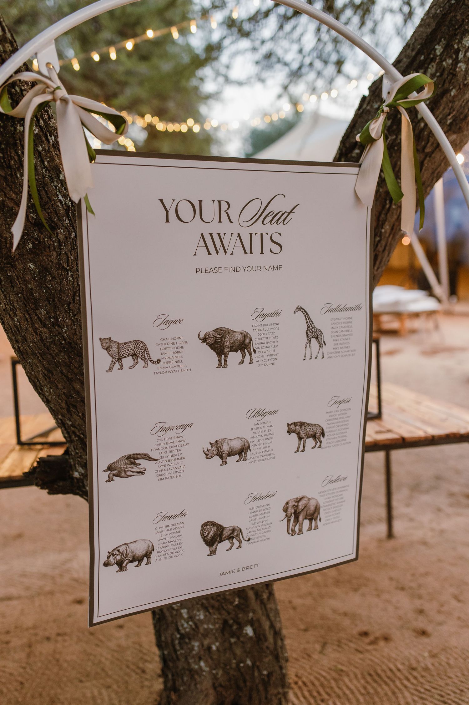 Wedding seating chart displays with animal illustrations hanging from tree branches at an outdoor venue.