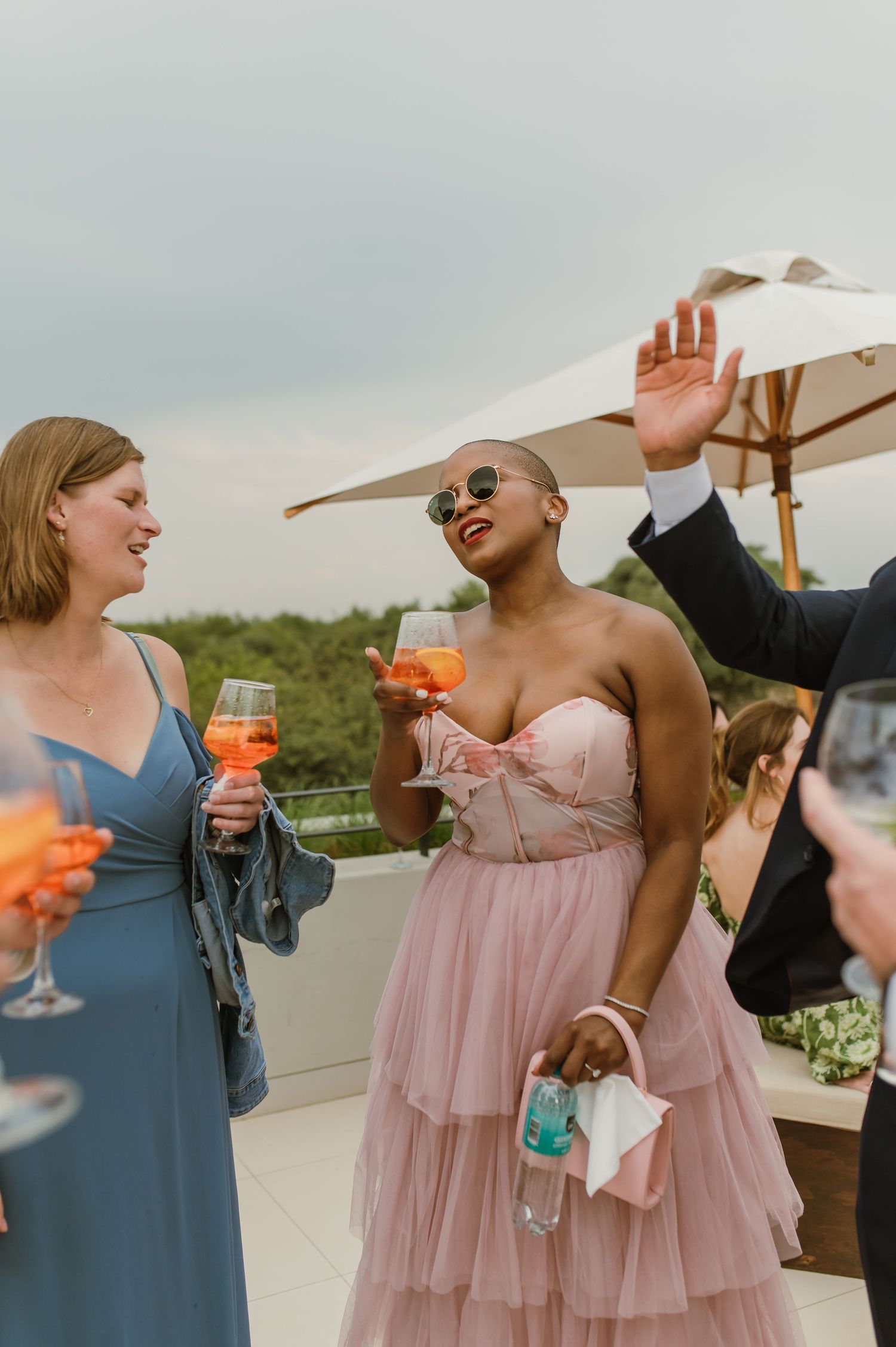 Wedding guests in formal attire toasting with colorful cocktails on a rooftop.