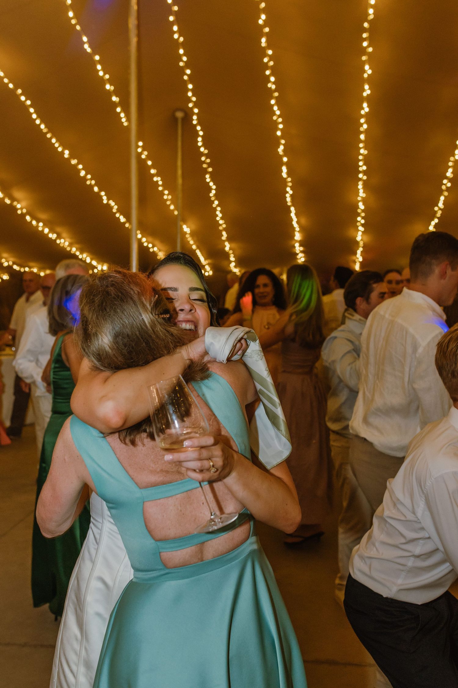 Wedding guests sharing embraces while dancing under string lights at reception.