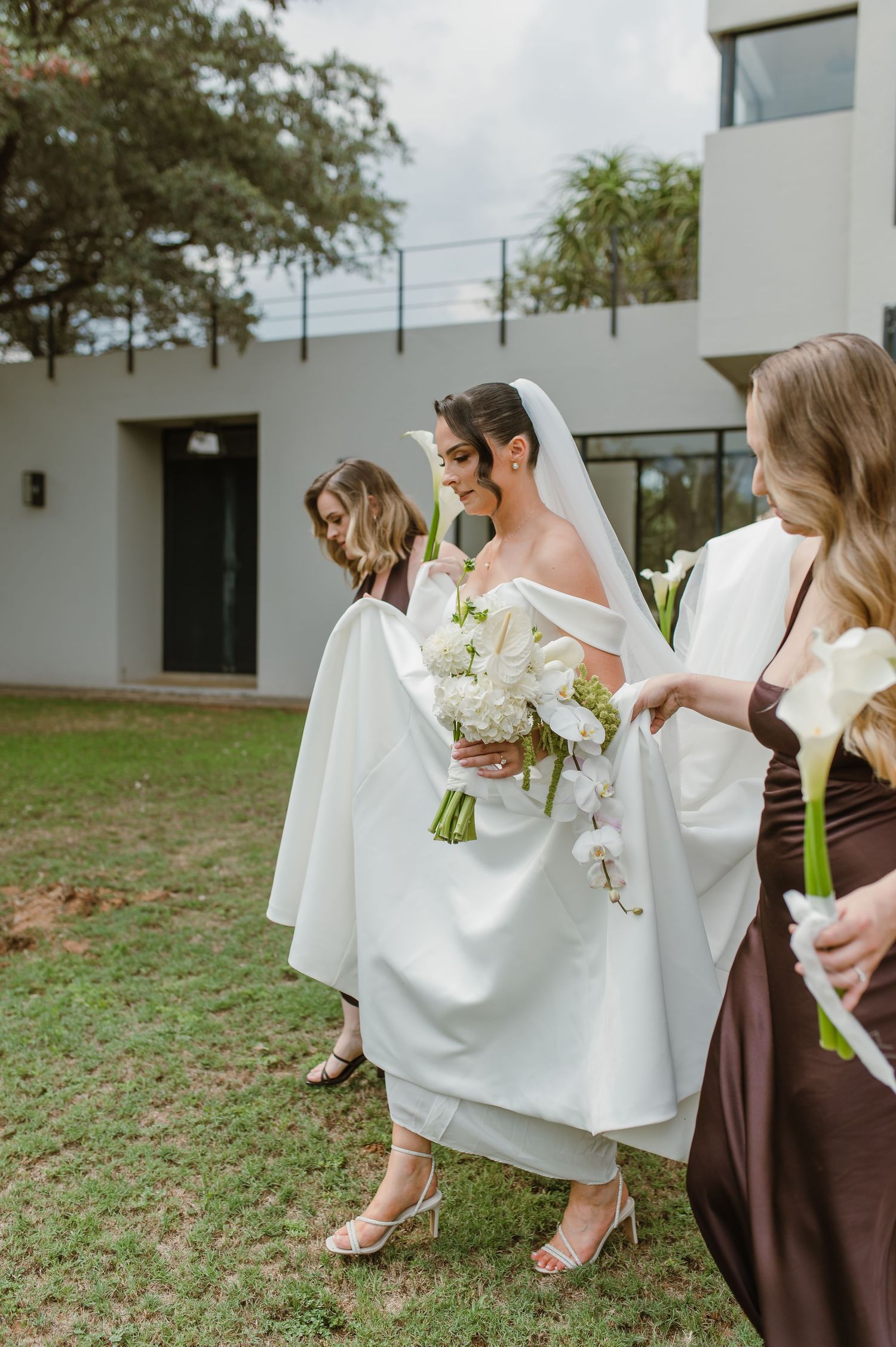 Wedding party walking outdoors with bride in white gown carrying bouquet of white flowers.